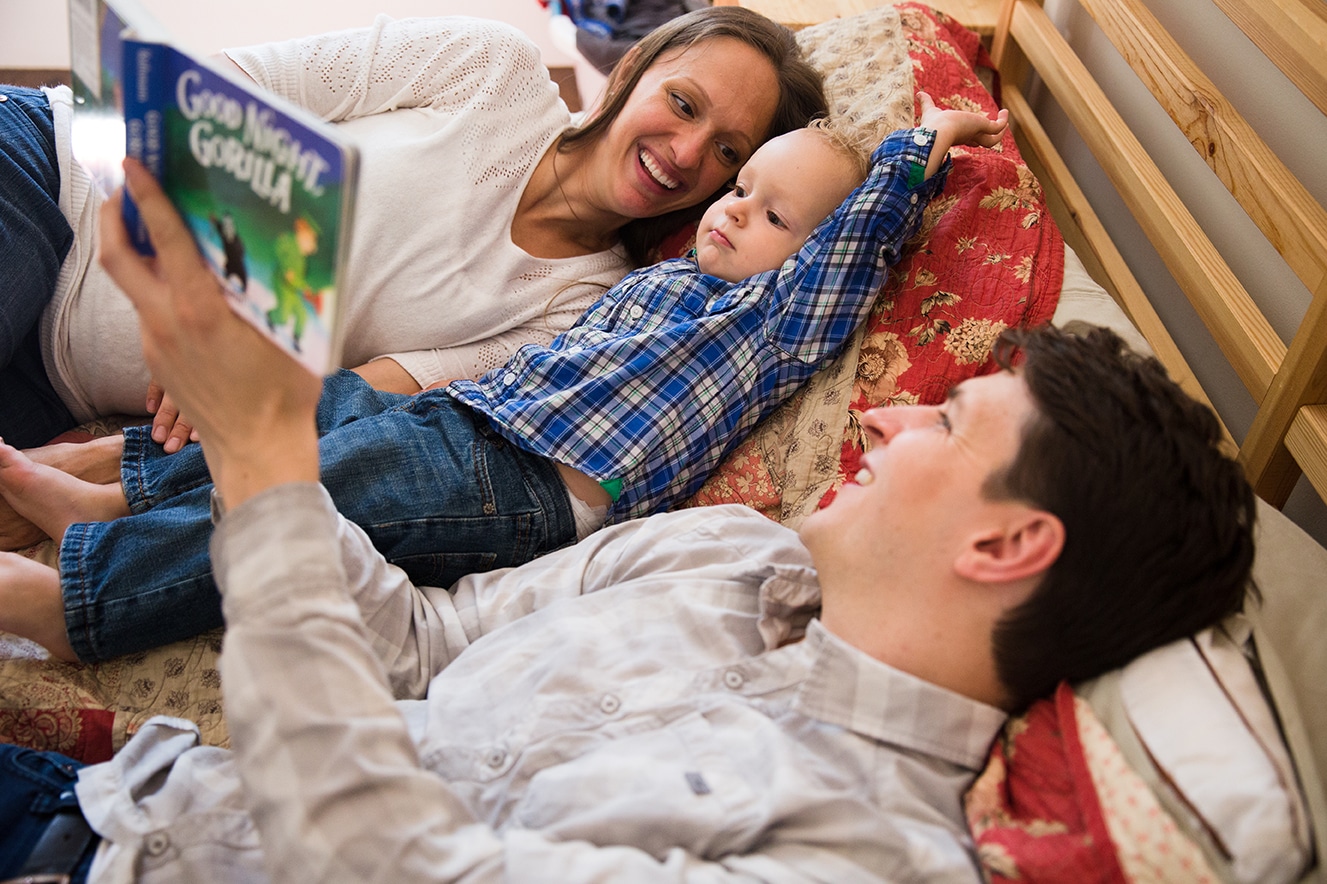 A lifestyle photograph of a family reading books together in bed during their in home family session in Boston