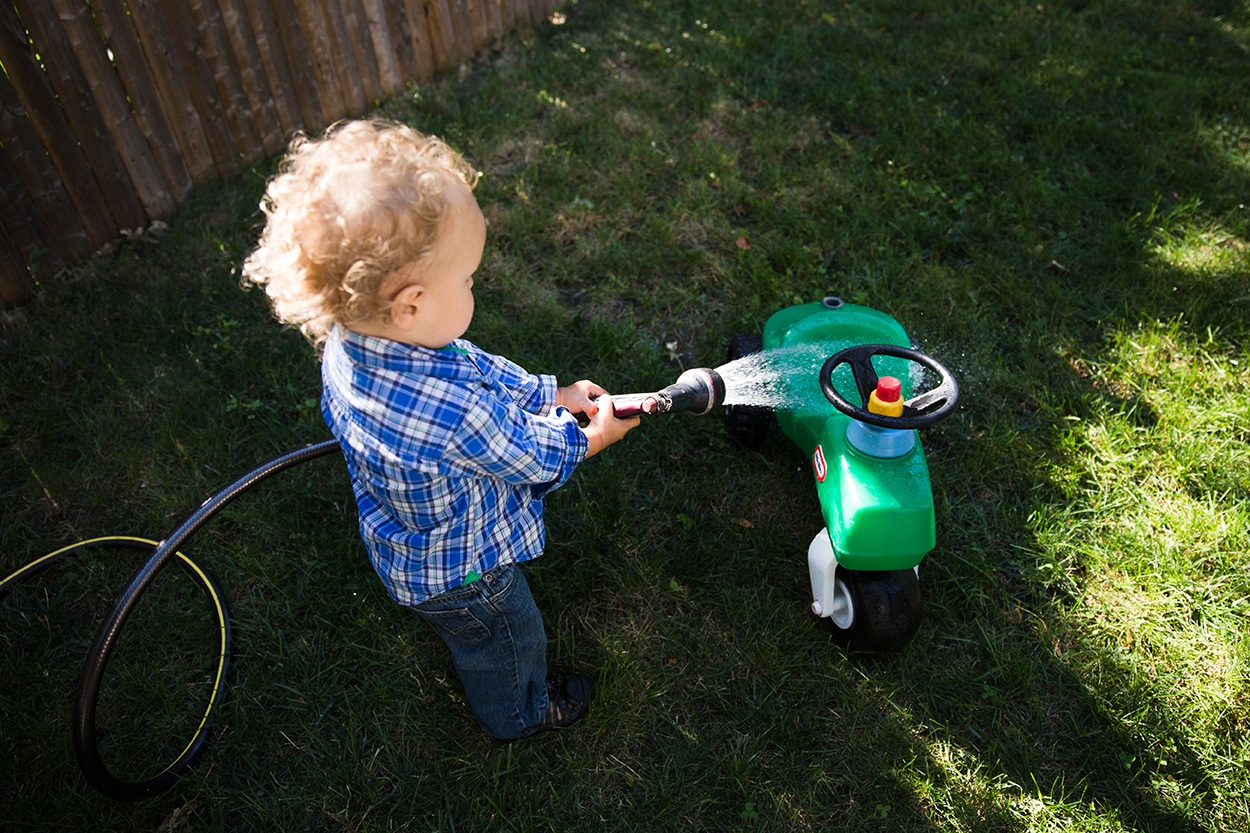 A lifestyle photograph of a boy washing his toy tractor in the yard during an in home family session in Boston