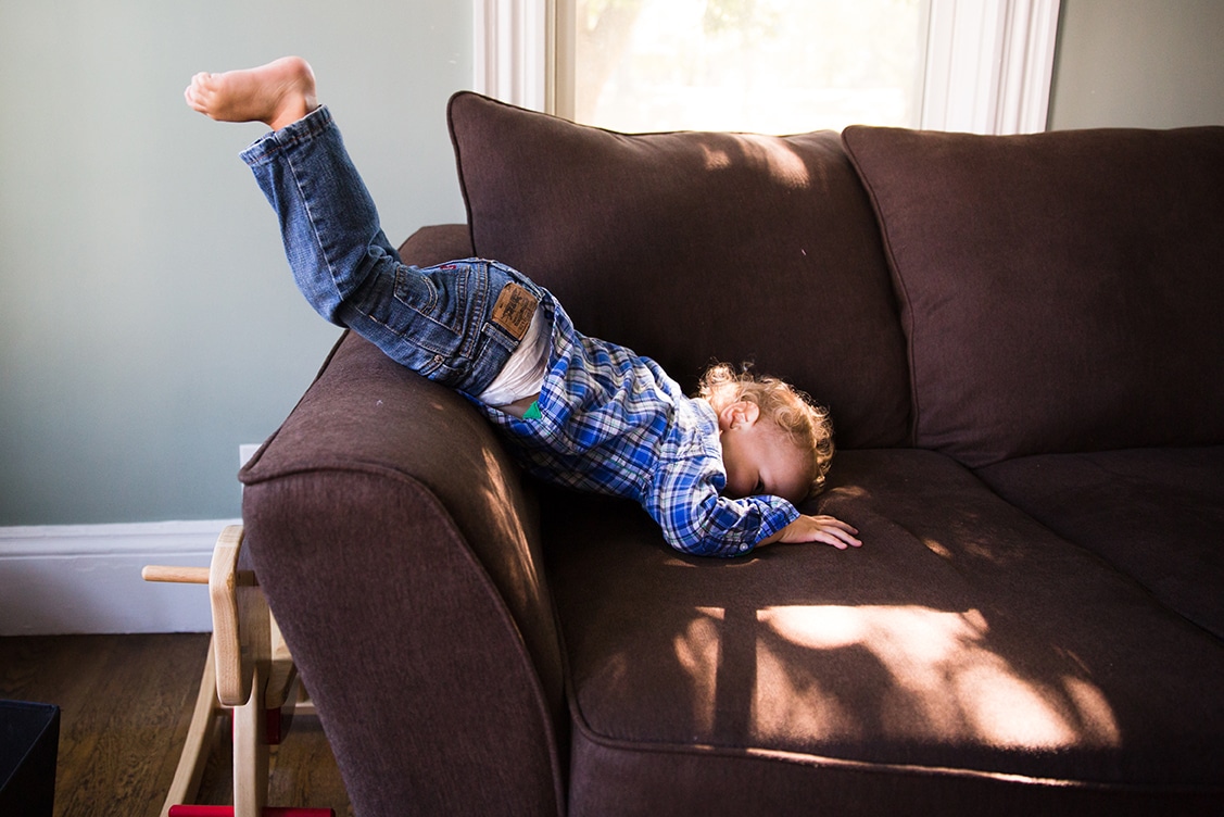 A documentary photograph of a toddler playing on the couch during an in home family session in Boston