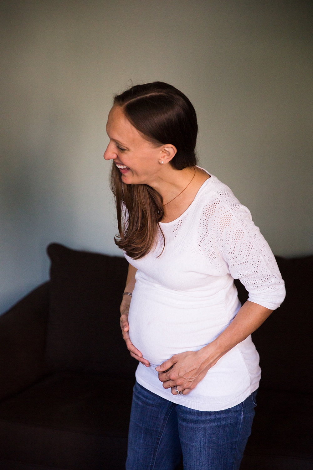 A lifestyle photograph of an expecting mother laughing during an in home family session in Boston