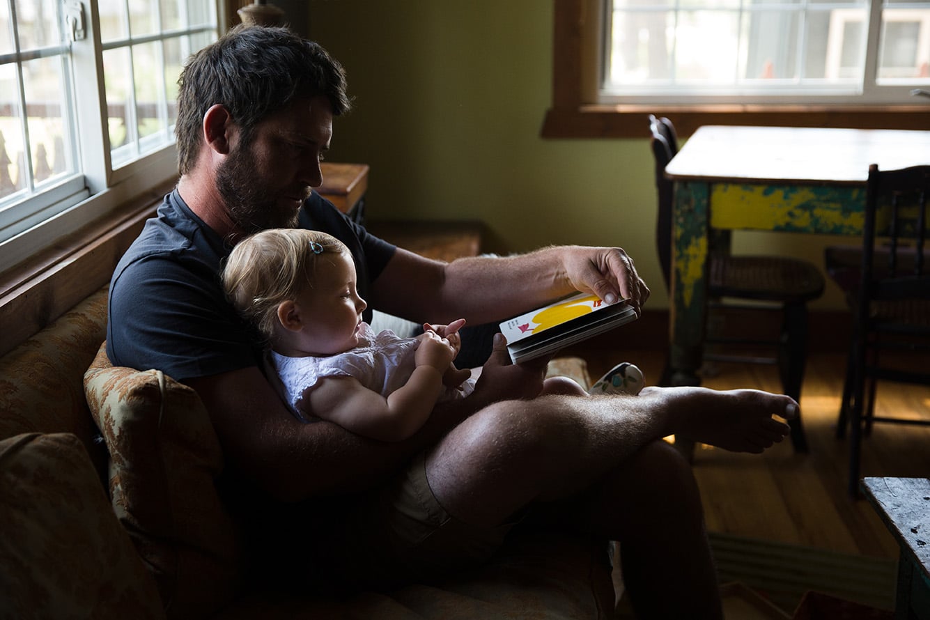 A documentary photograph of a dad reading a book to his daughter during their evergreen family session at their home in Colorado