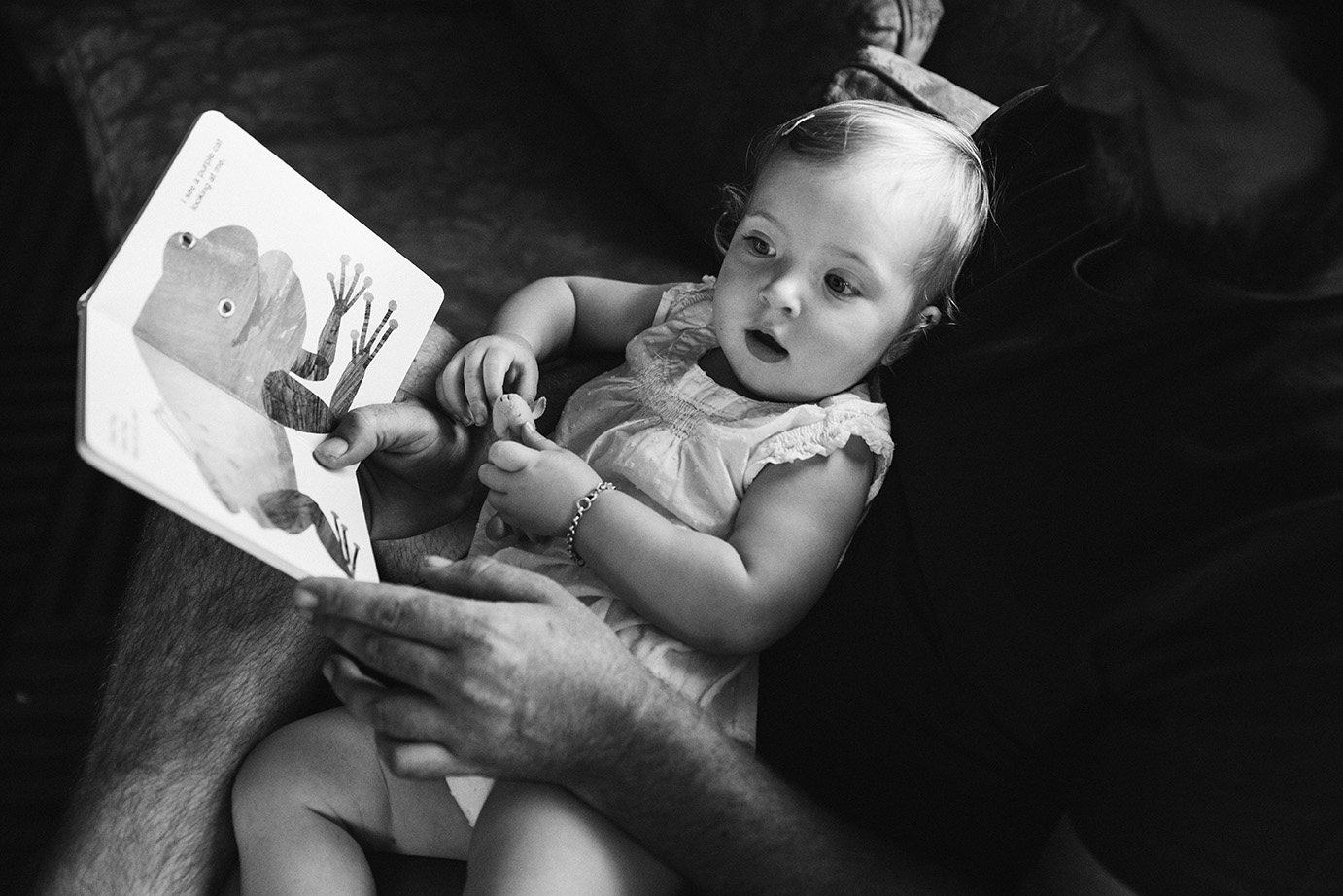 A documentary photograph of a toddler reading a book with her dad during their evergreen family session at home in Colorado
