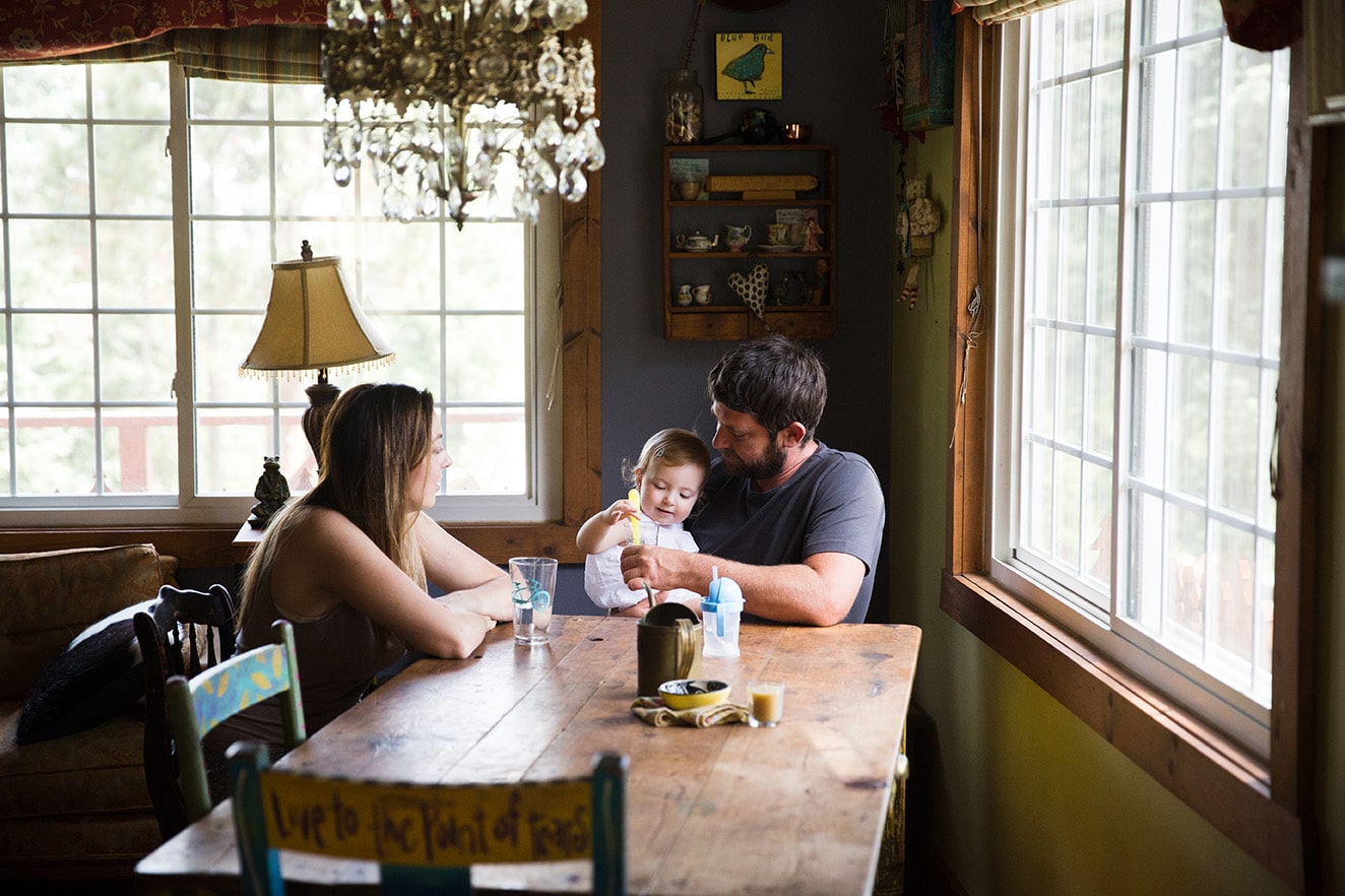 A documentary photograph of a toddler having a snack with her parents during their evergreen family session at home in Colorado
