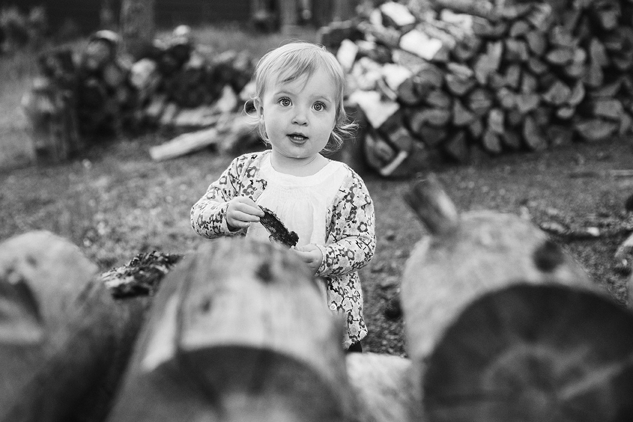 A lifestyle portrait of a toddler playing near a wood pile during an evergreen family session at home in Colorado