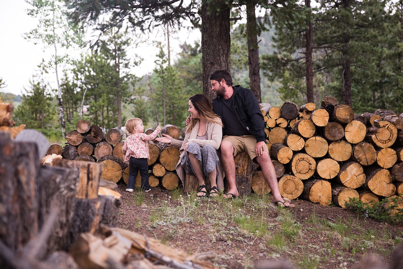 A lifestyle photograph of a family sitting on a wood pile during their evergreen family session at home in Colorado