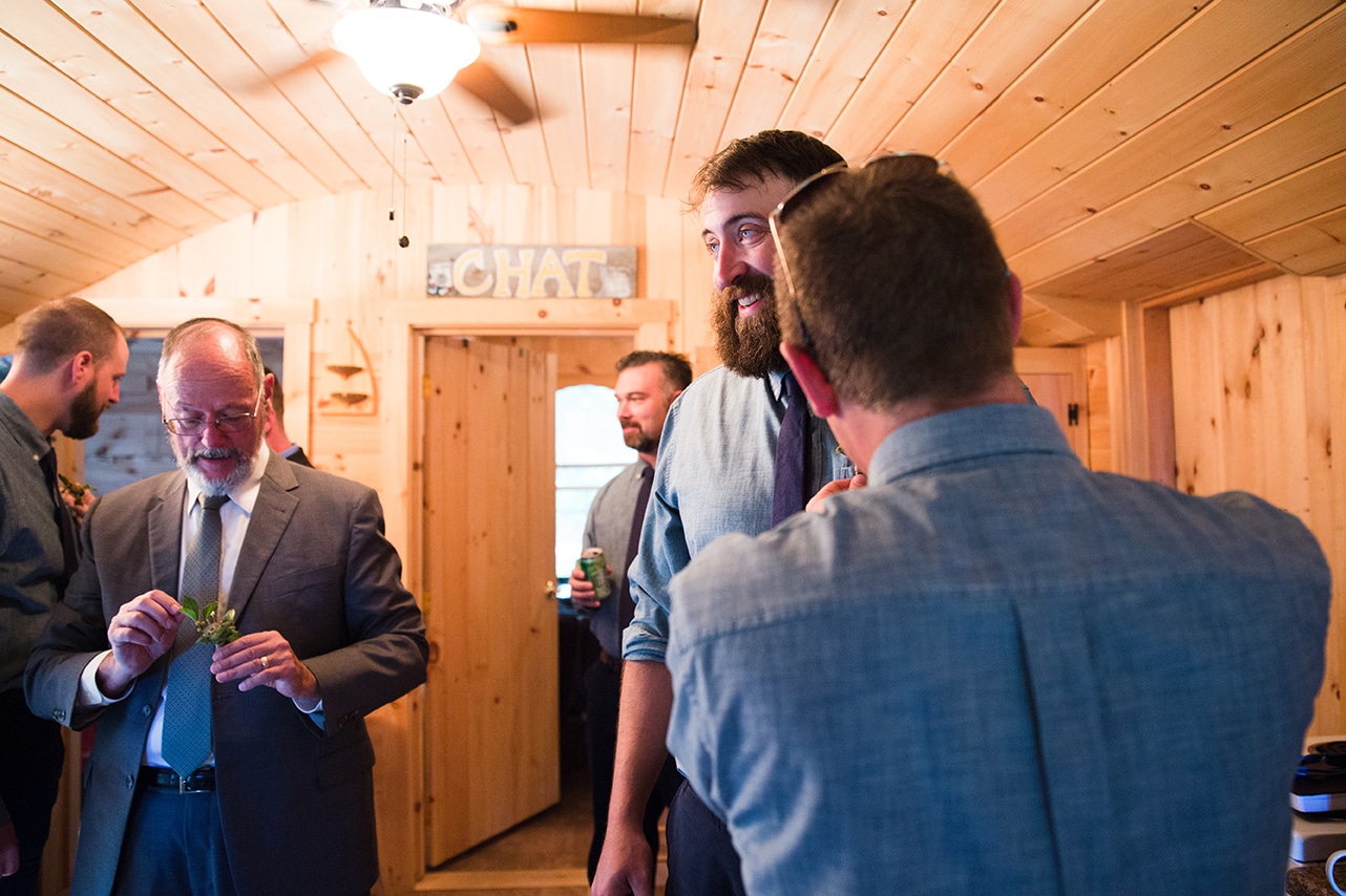 A documentary photograph of Groomsmen putting on their boutonnieres before a Kingsley Pines Camp Wedding in Maine 