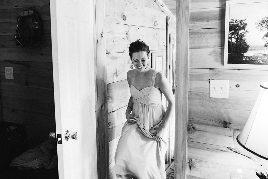 A documentary photograph of a bridesmaid laughing as she gets ready for a Kingsley Pines Camp wedding in Maine