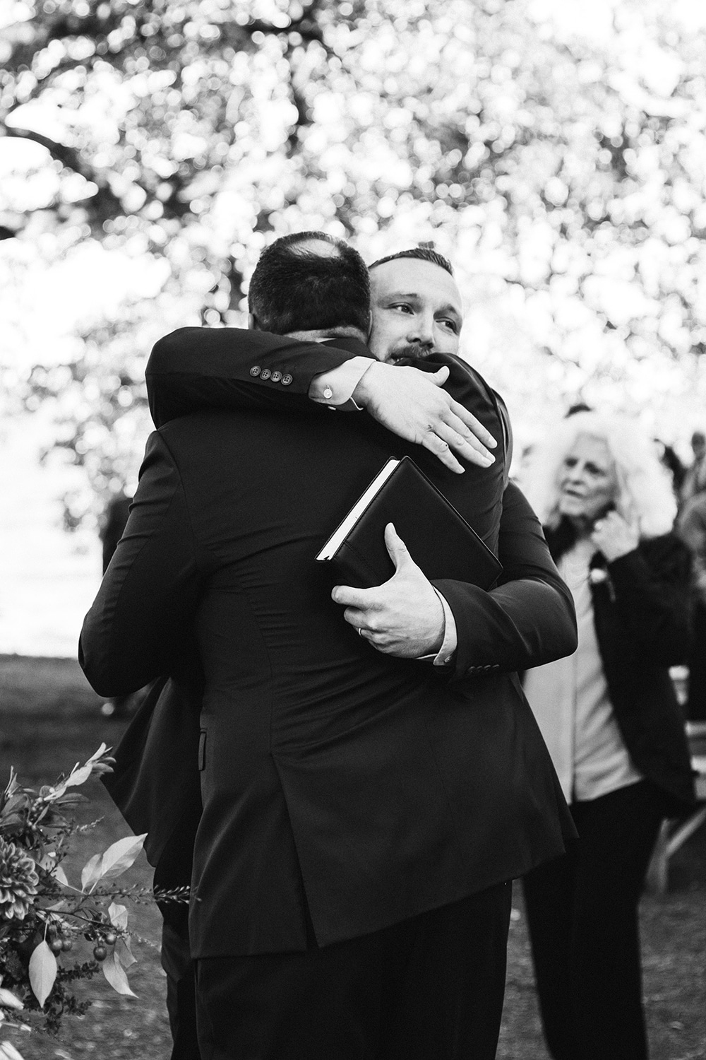 A documentary photograph of the officiant hugging the groom after his outdoor wedding ceremony at Kingsley Pines Camp in Maine