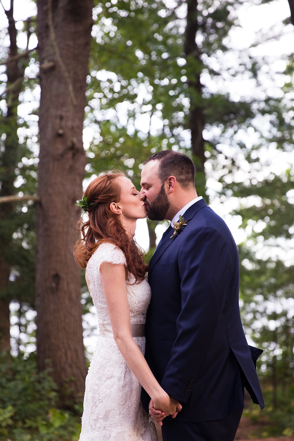 A sweet and natural portrait of a bride and groom kissing in the woods during their Kingsley Pines Camp wedding in Maine