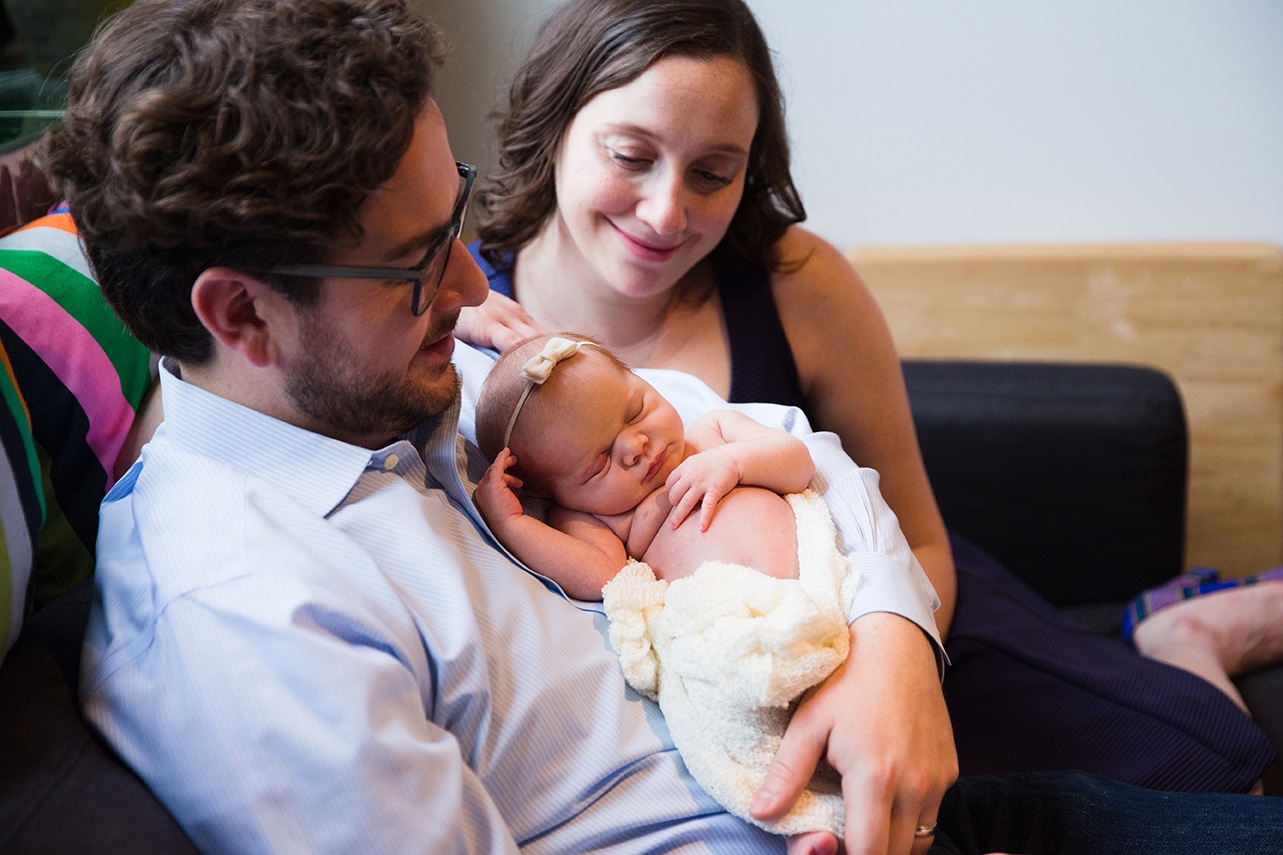 A lifestyle photograph of a mother and father holding their new baby girl during an in home newborn session in the Jamaica Plain neighbourhood of Boston, Massachusetts
