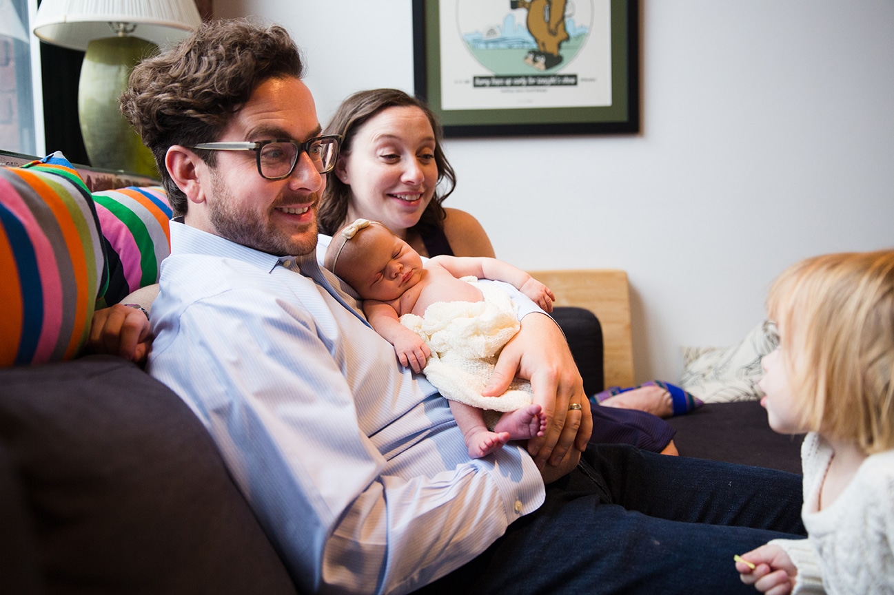A lifestyle photograph of a family in their living room during an in home newborn session in the Jamaica Plain neighbourhood of Boston, Massachusetts