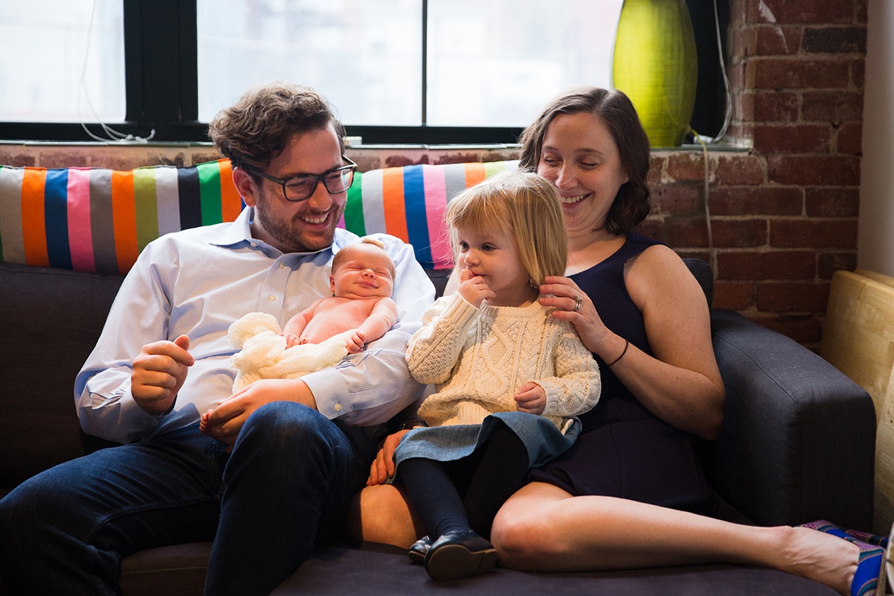 A lifestyle photograph of a family sitting together on the couch during an in home newborn session in the Jamaica Plain neighbourhood of Boston, Massachusetts