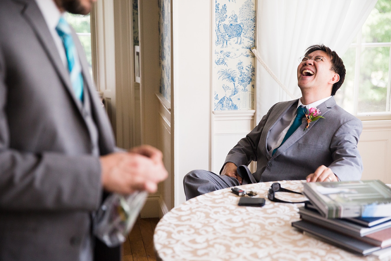 A documentary photograph of a groomsman laughing while they get ready for a Lyman Estate Wedding in Boston, Massachusetts