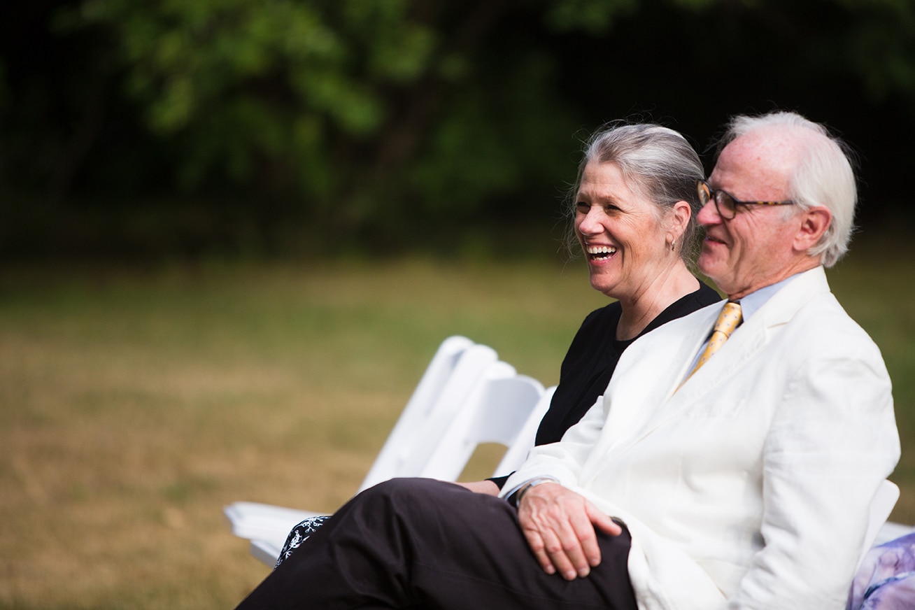 A documentary photograph of the Groom's parents smiling during an outdoor wedding ceremony at the Lyman Estate in Boston, Massachusetts