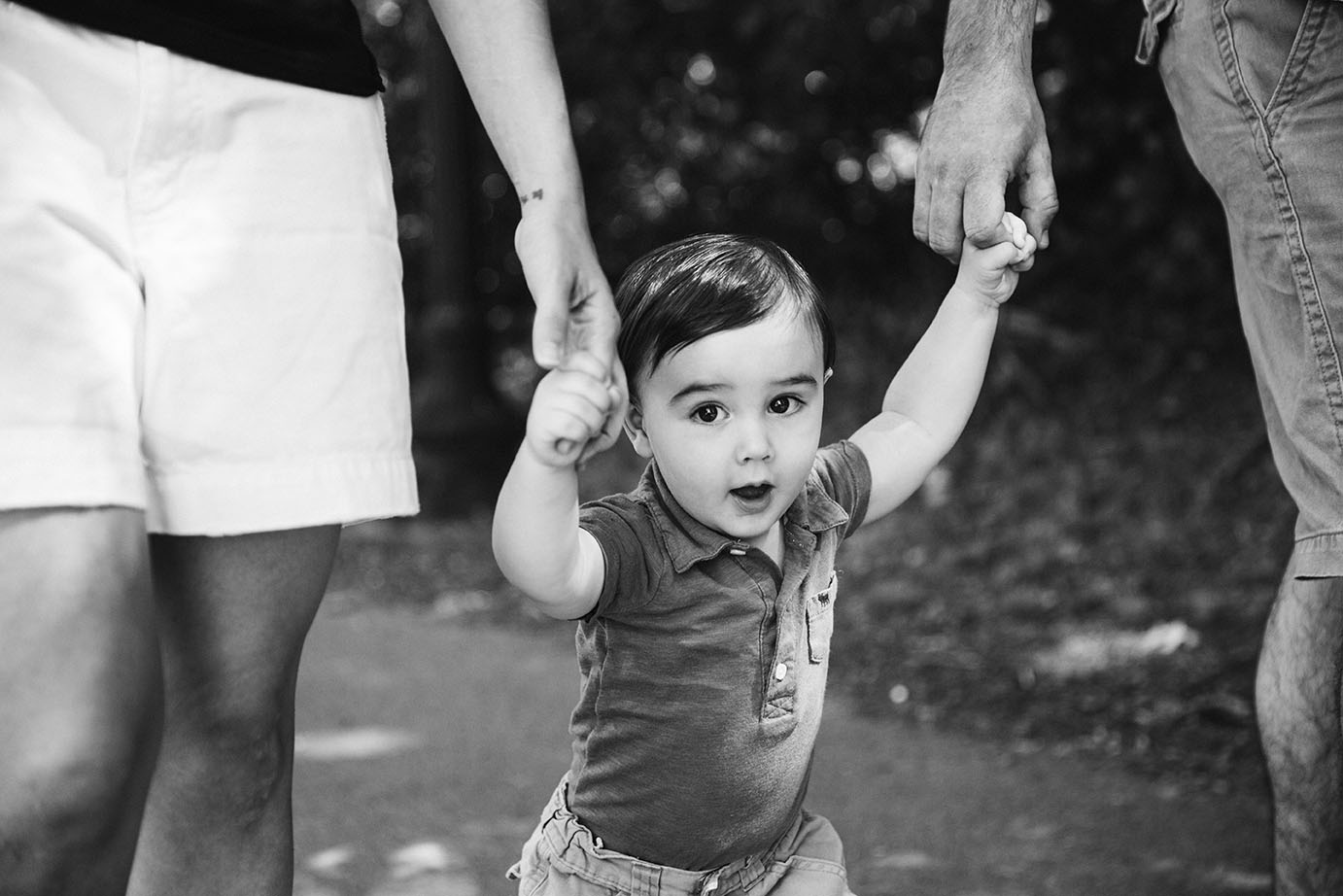 A lifestyle portrait of a baby holding his parents hands as they walk through Jamaica Pond during a Boston Family Session.