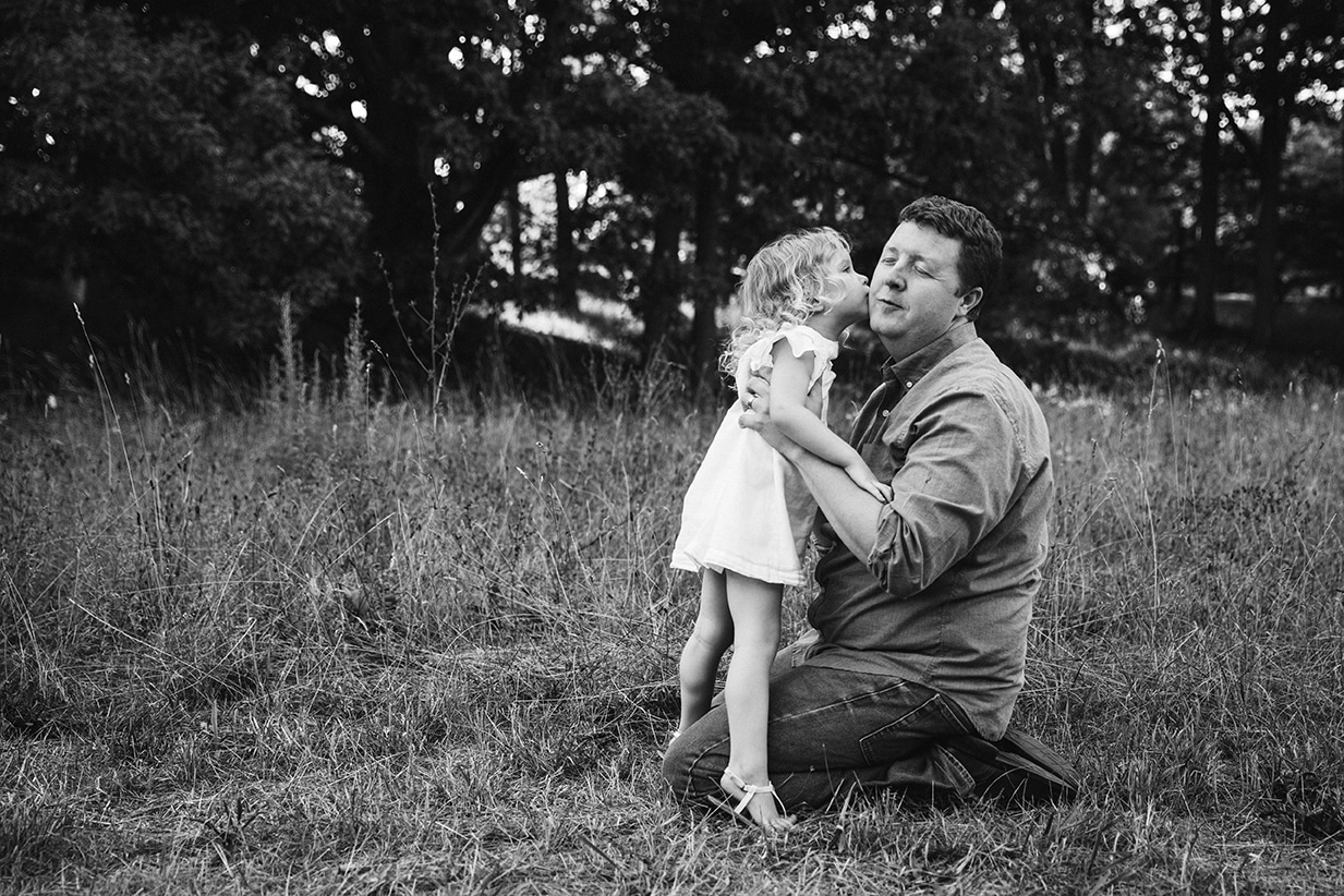 A documentary photograph of a little girl kissing her dad during their Arnold Arboretum family session in Boston, Massachusetts