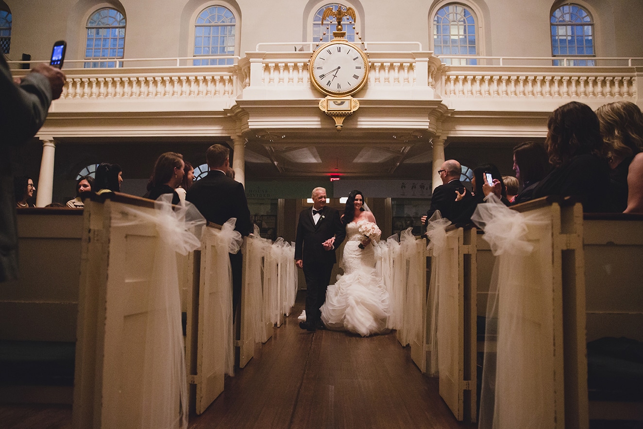 A documentary photograph of a bride walking down the aisle with her father during her old south meeting house and marliave wedding in Boston, Massachusetts