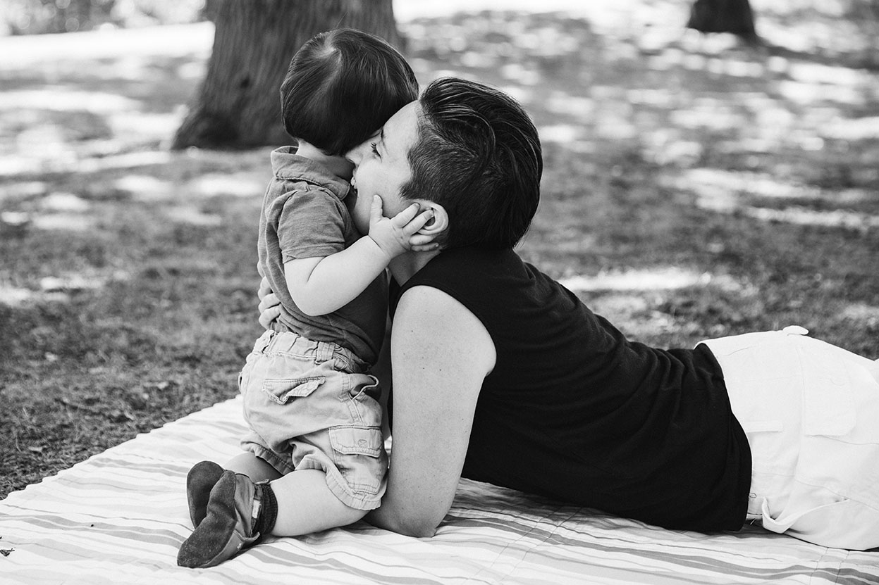 A documentary photograph of a baby hugging his momma as they lay on a blanket during their Jamaica Pond family session