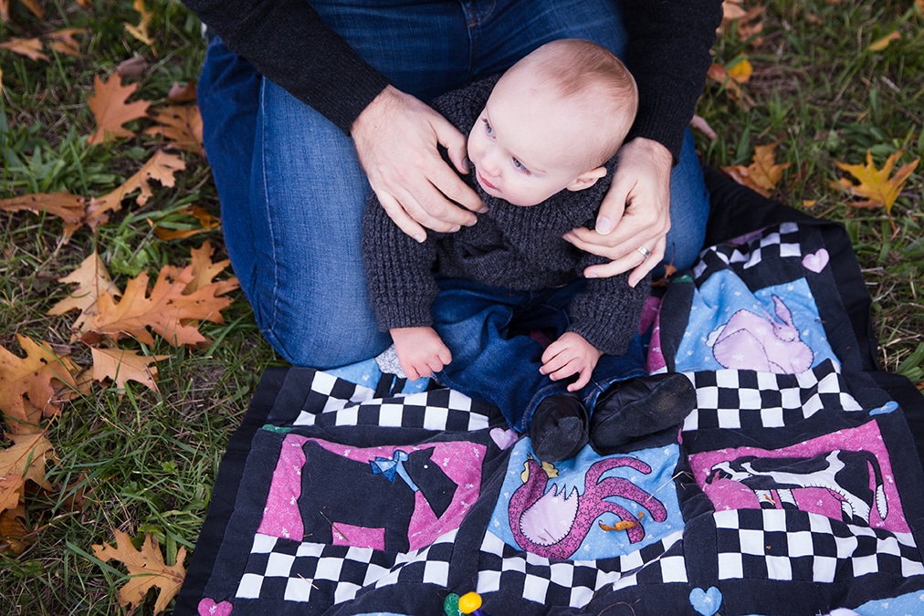 A documentary photograph of a baby sitting on a blanket with his father during their Arboretum Family Session in Boston, Massachusetts