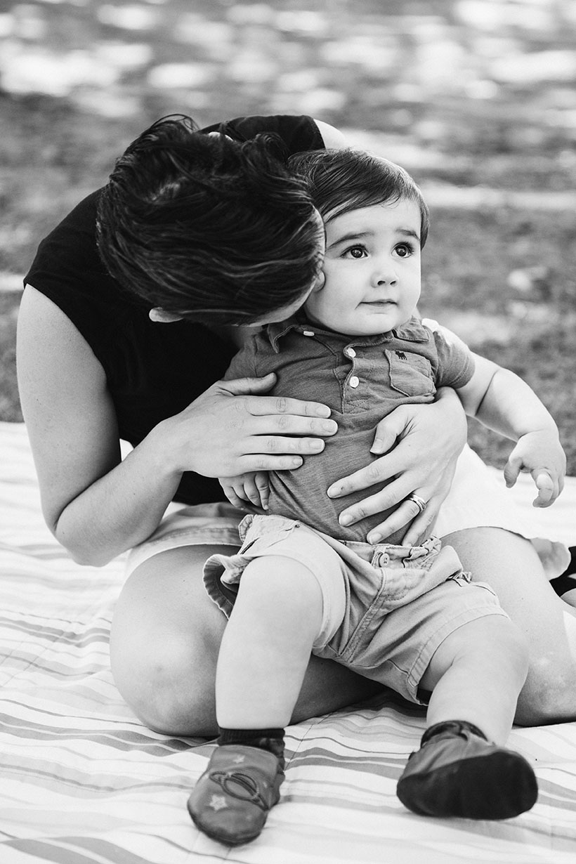 A documentary photograph of a mother hugging her son as they sit on blanket during their Jamaica Pond family session