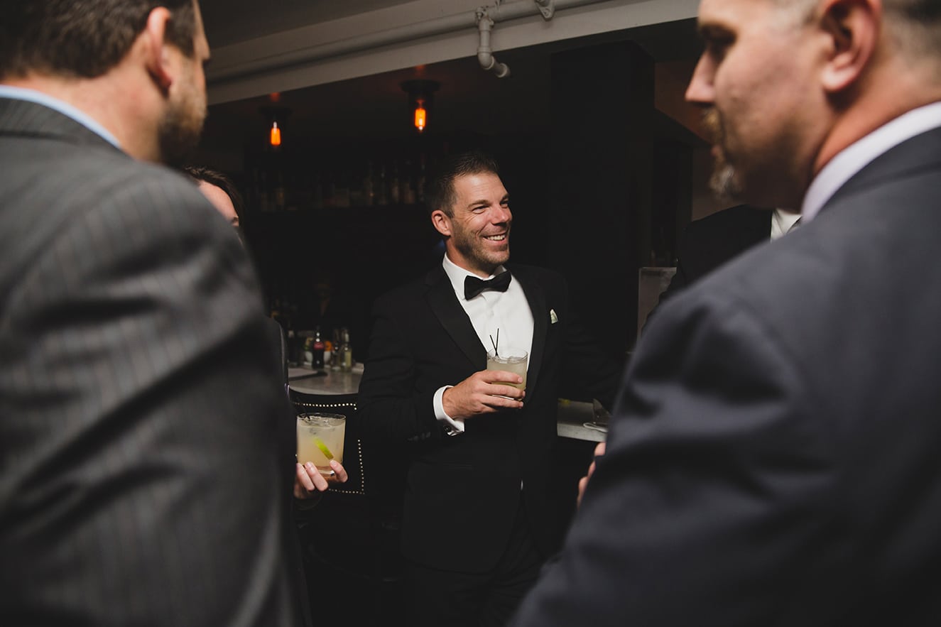 A documentary photograph of a groom talking and laughing with friends during his marliave wedding reception in Boston, Massachusetts