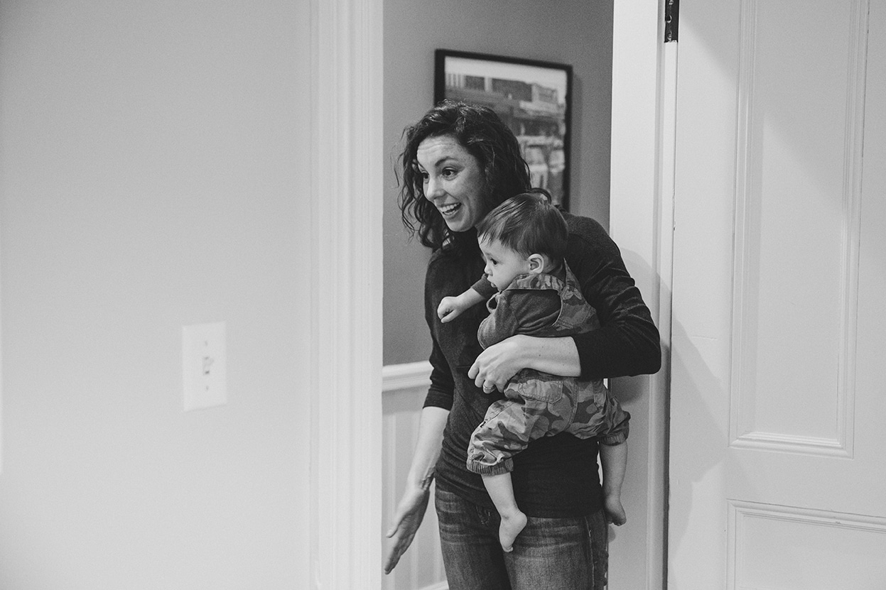 A documentary photograph of a mom calling the dog while holding her son during an in home family session in Boston, Massachusetts