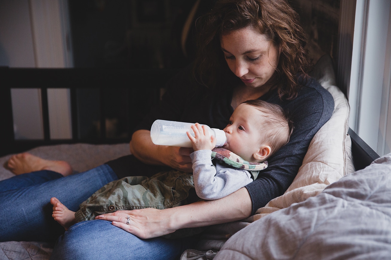 A documentary photograph of a mom feeding her baby boy during an in home family session in Boston, Massachusetts