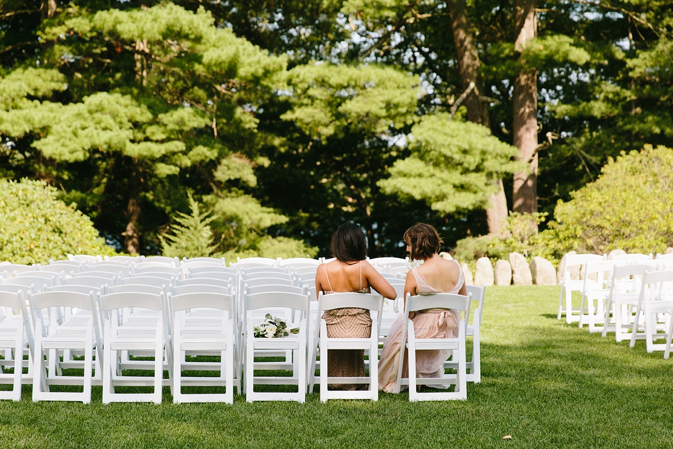 A documentary photograph of two bridesmaids sitting at the ceremony site before a Moraine Farm wedding in Beverly, Massachusetts