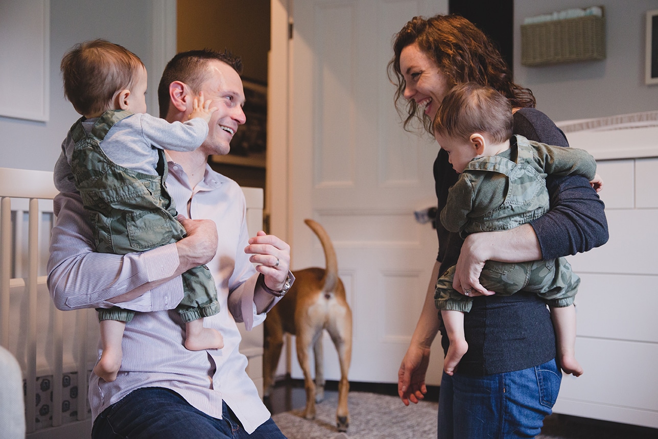 A documentary photograph of parents laughing together while holding their twin boys during an in home family session in Boston, Massachusetts