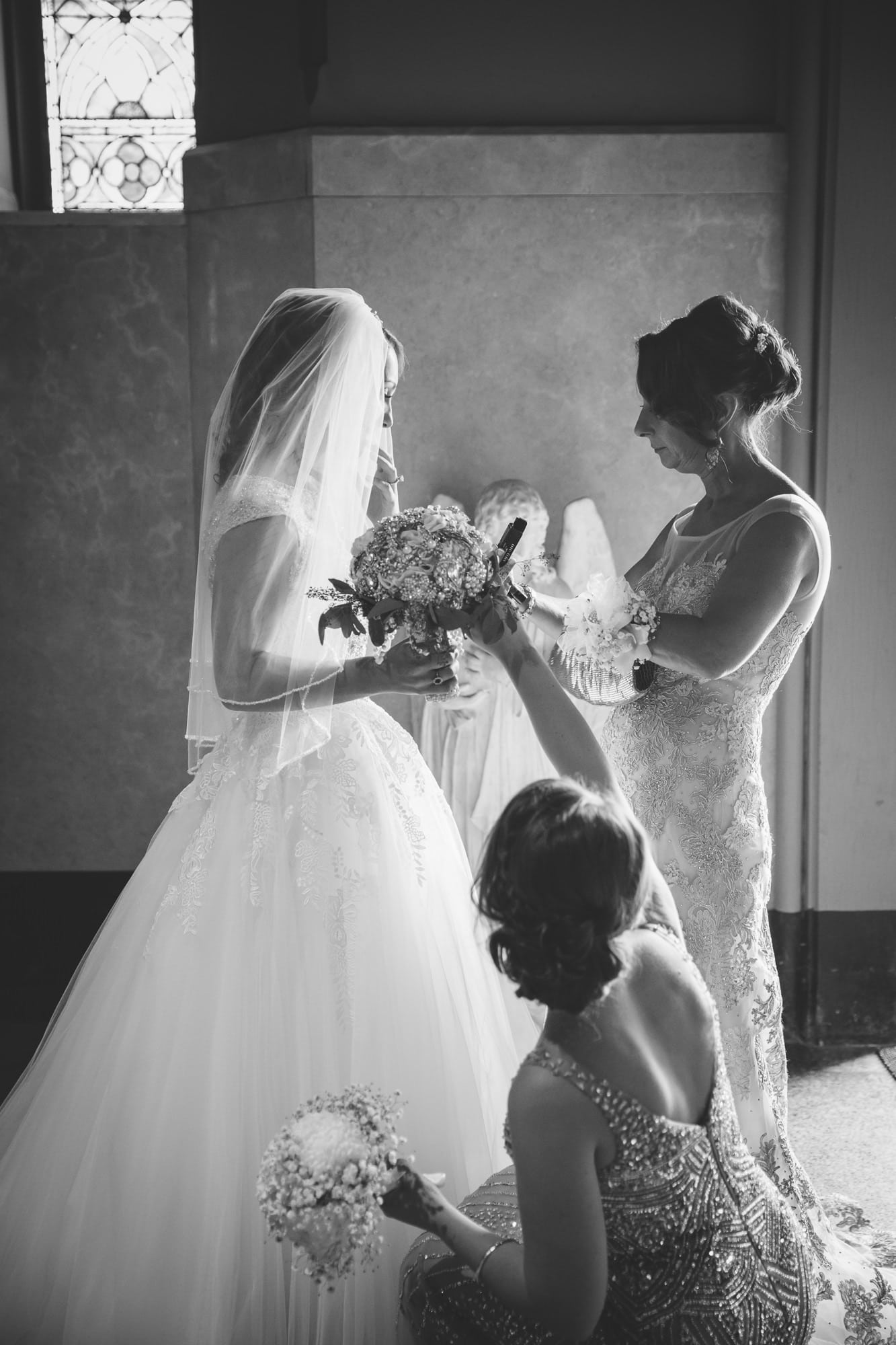 A documentary photograph of a bride's mother and sister preparing her to walk down the aisle of the Cathedral of the Holy Cross during her State Room Wedding in Boston, Massachusetts