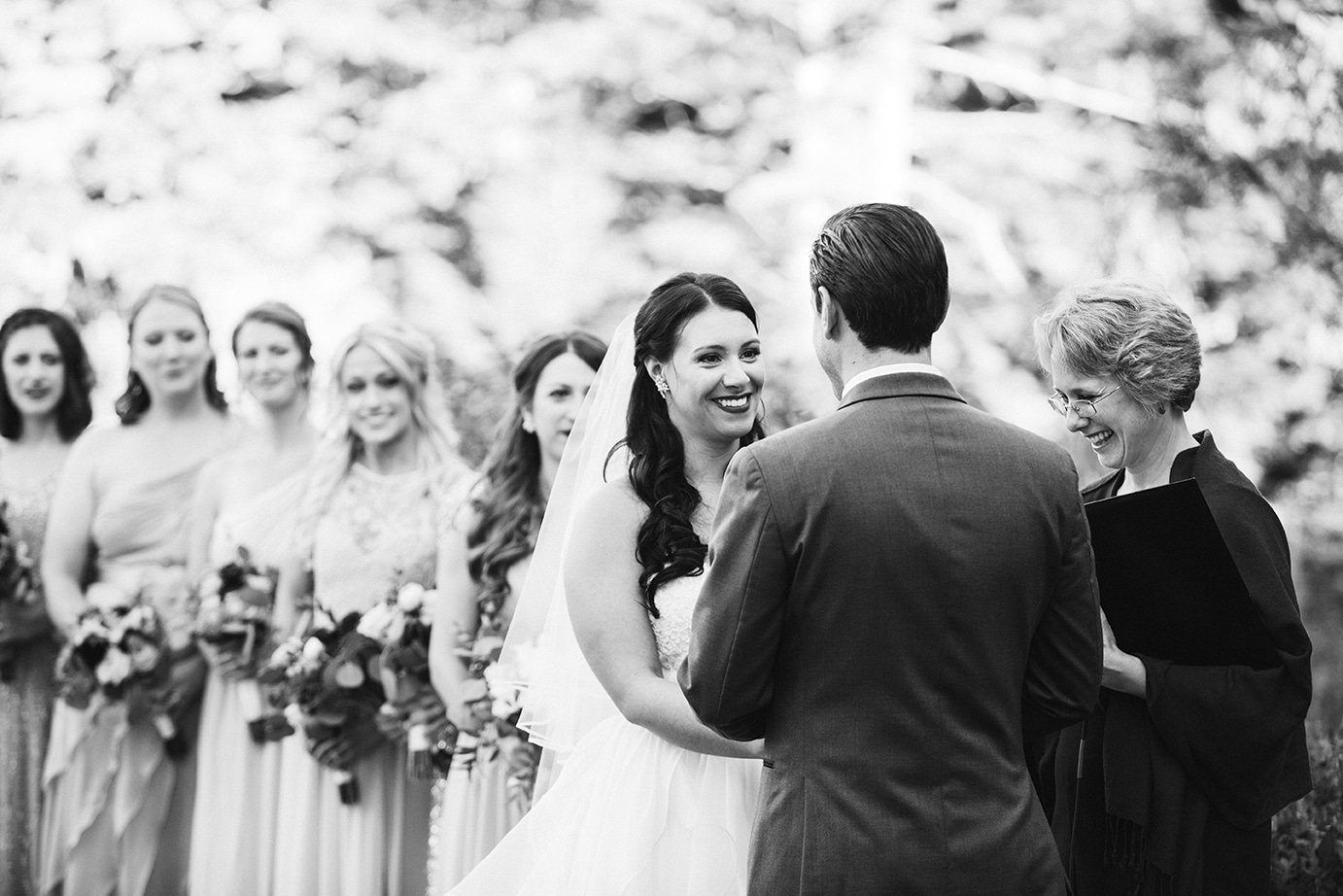 A documentary photograph of a bride smiling at her groom during their outdoor wedding ceremony at Harrington Farm in Princeton, Massachusetts