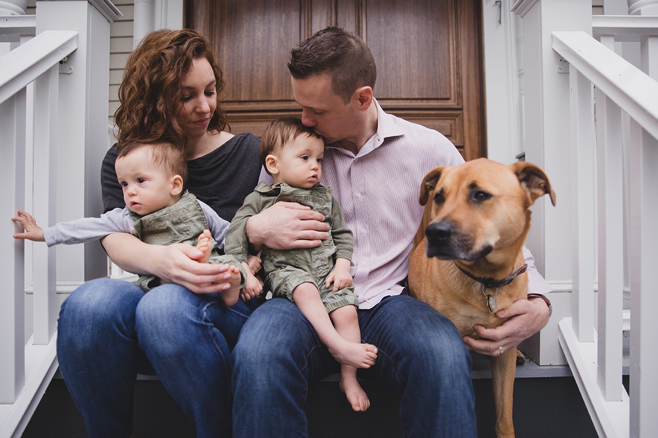 A documentary photograph of a family sitting on the porch with their dog during an in home family session in Boston, Massachusetts