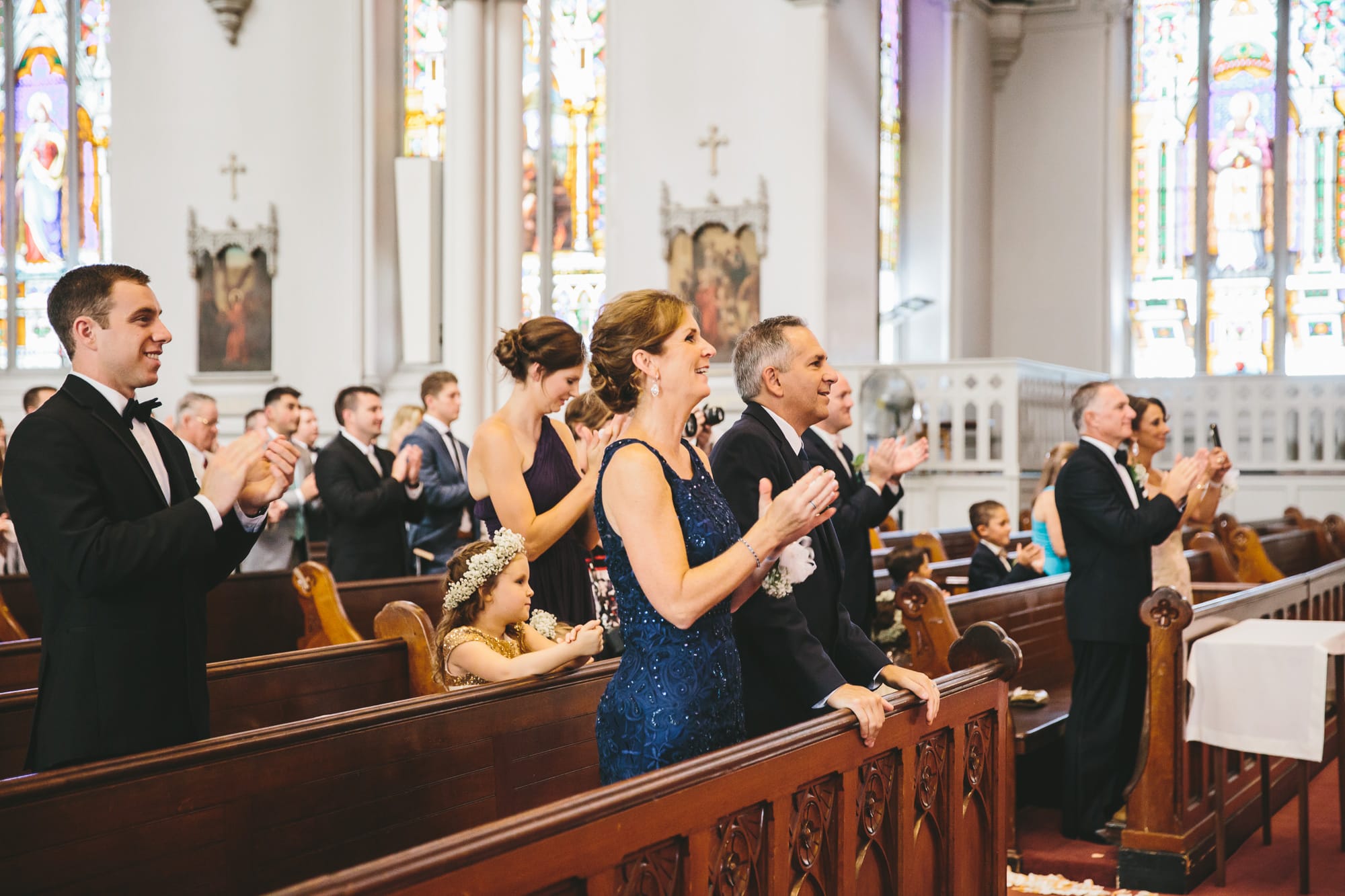 A documentary photograph of family and friends clapping during a wedding ceremony at the Cathedral of the Holy Cross
