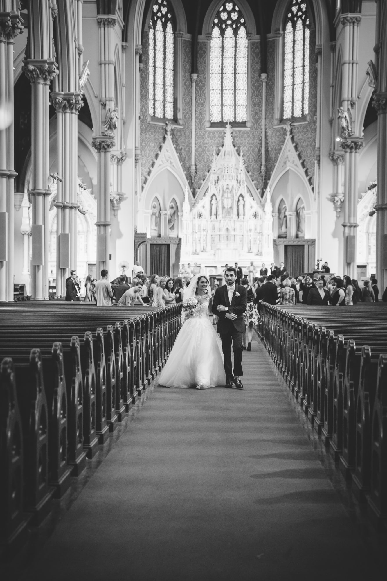 A documentary photograph of couple walking down the aisle of the Cathedral of the Holy Cross after their wedding ceremony