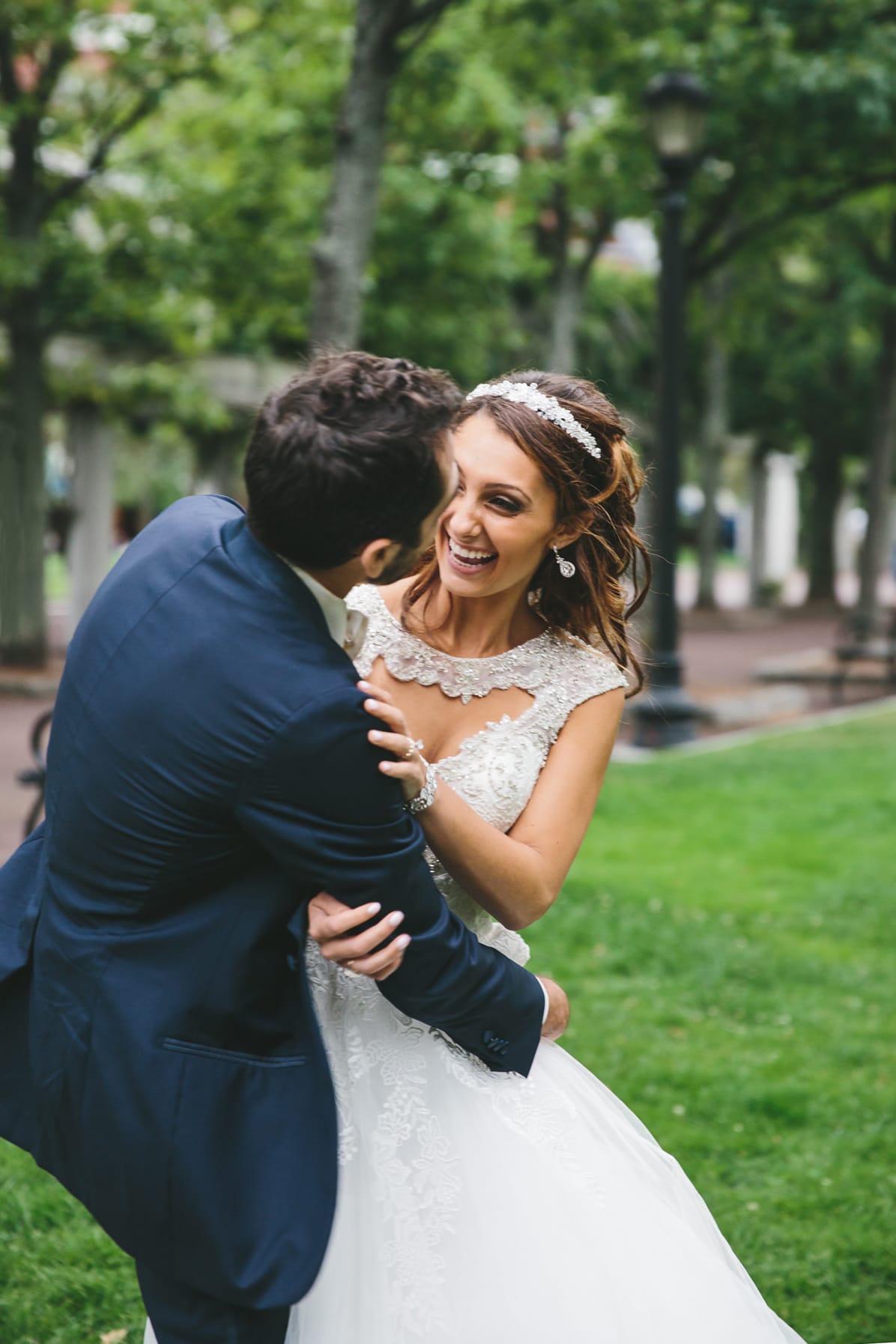 A documentary photograph of a bride and groom laughing together at the Boston Public Gardens during their State Room Wedding