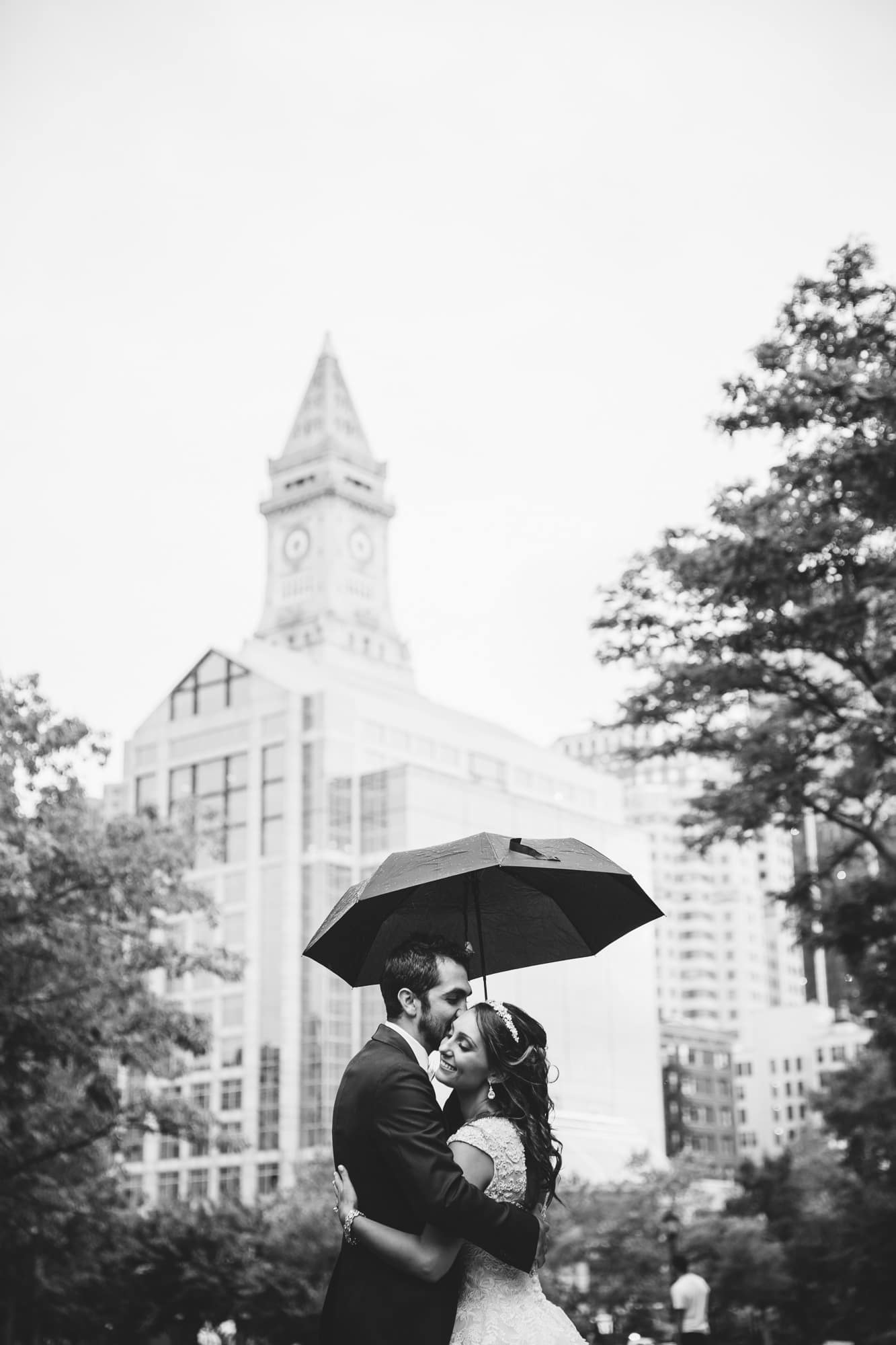 A documentary photograph of a couple hugging under an umbrella during a rainy State Room Wedding in Boston, Massachusetts