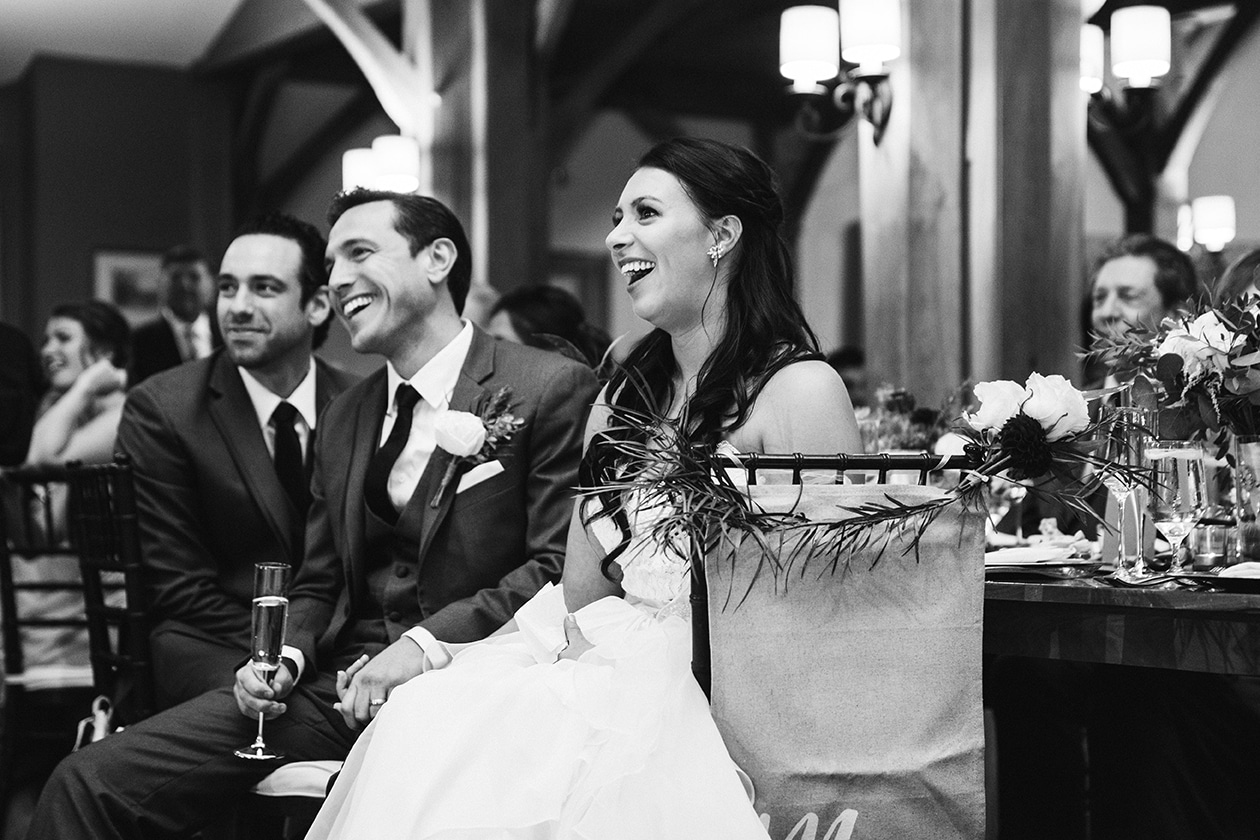 A documentary photograph of a bride and groom smiling and laughing during the wedding toasts at their Harrington Farm Wedding in Princeton, Massachusetts
