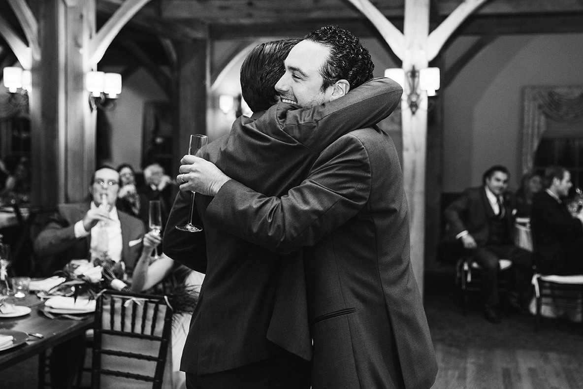 A documentary photograph of a groom hugging his brother after the wedding toasts of his Harrington Farm Wedding in Princeton, Massachusetts