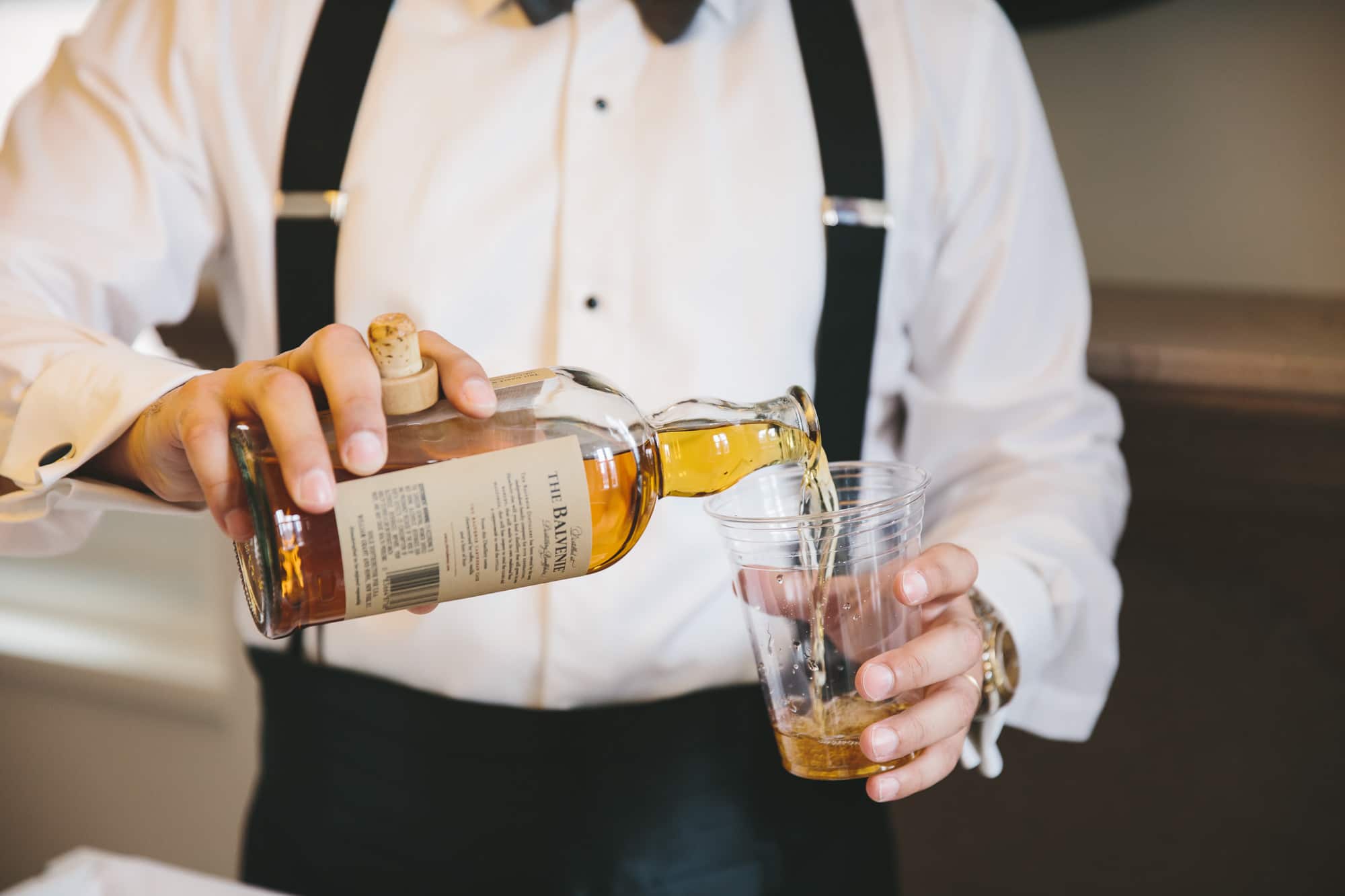 A groomsmen pours a drink during preparations at the Ames hotel before a state room wedding