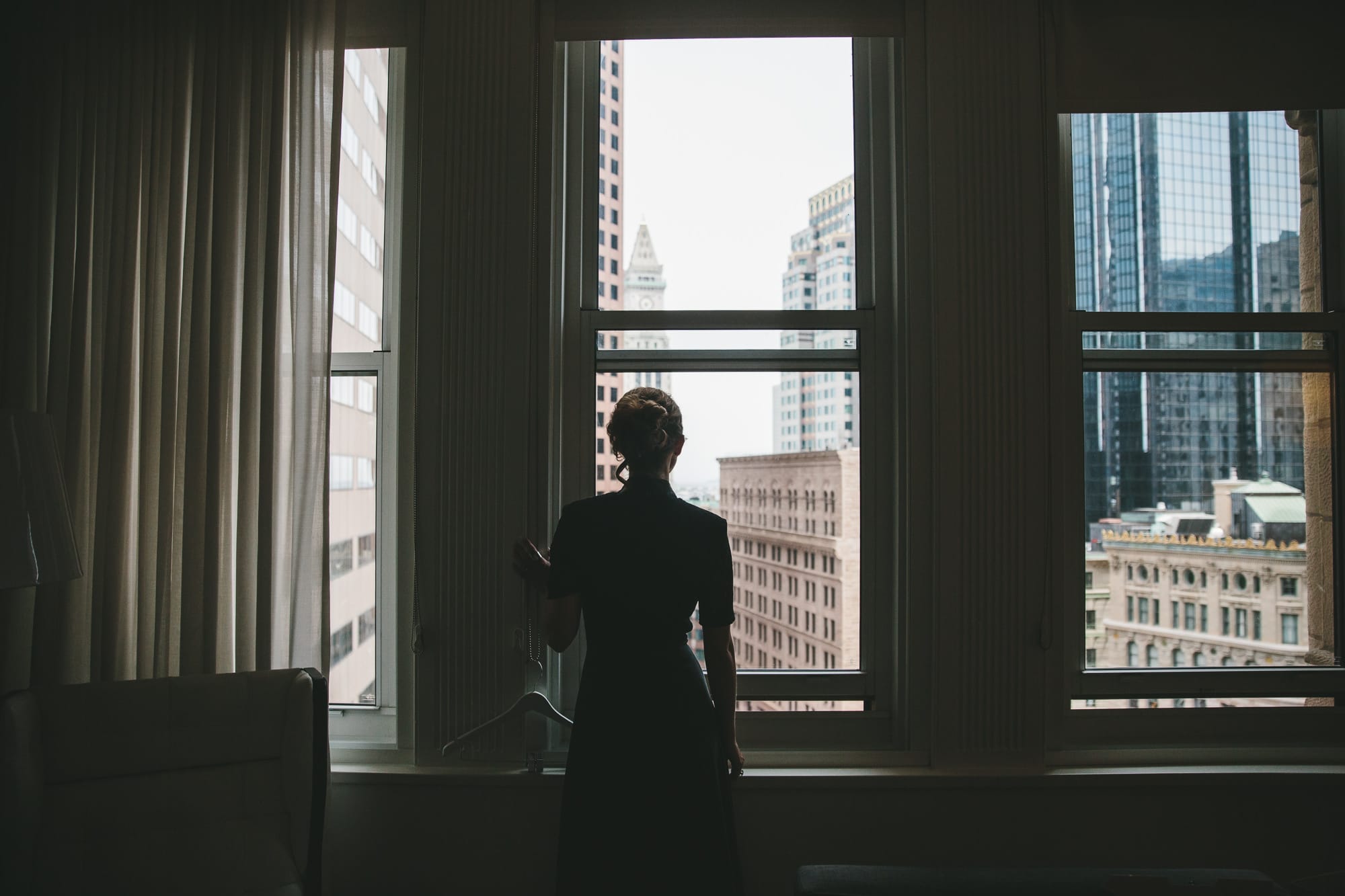 A portrait of a bridesmaids looking out the window of the Ames hotel before a State Room wedding