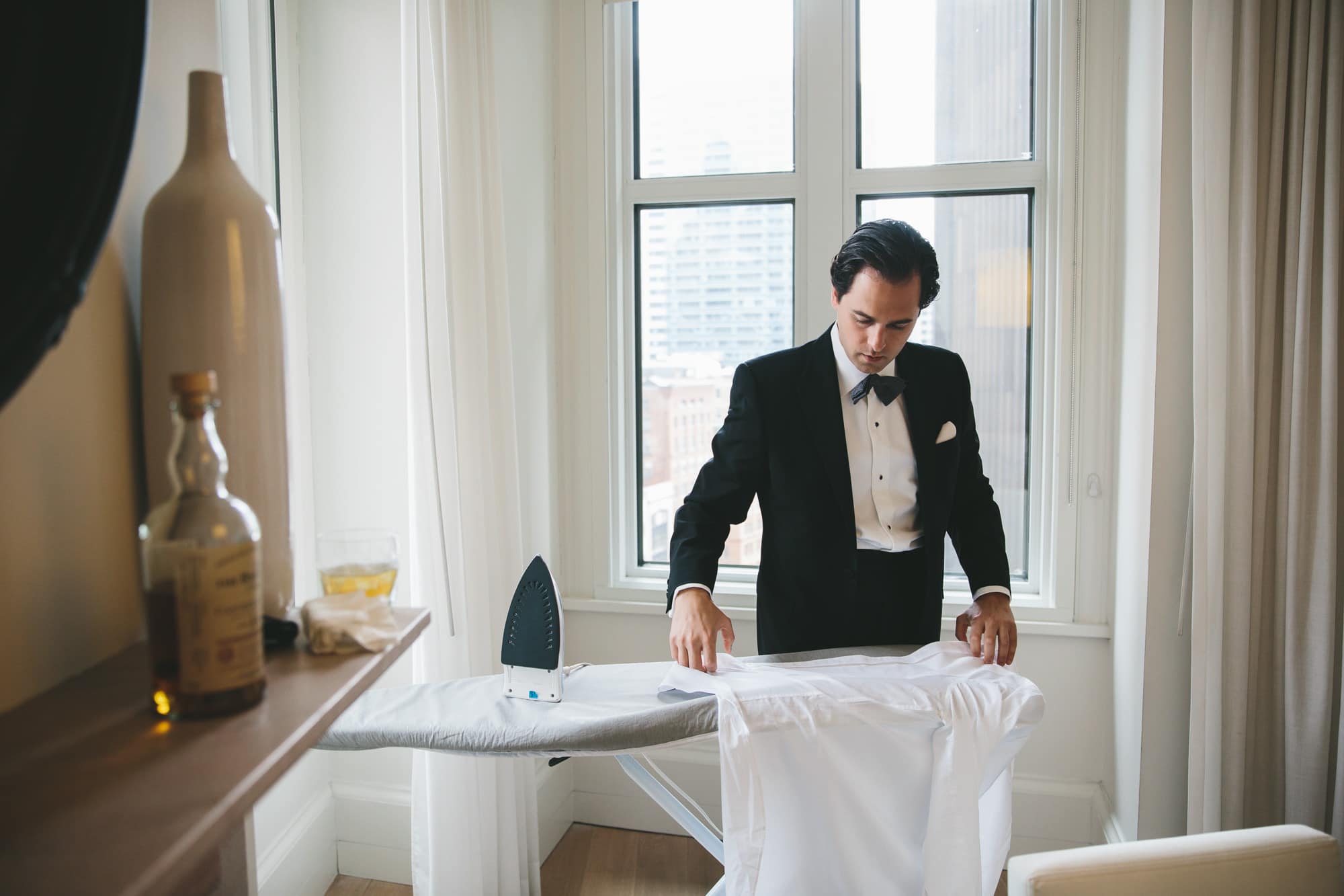 A documentary photograph of a groomsman ironing the grooms shirt at the Ames hotel before a State Room Wedding