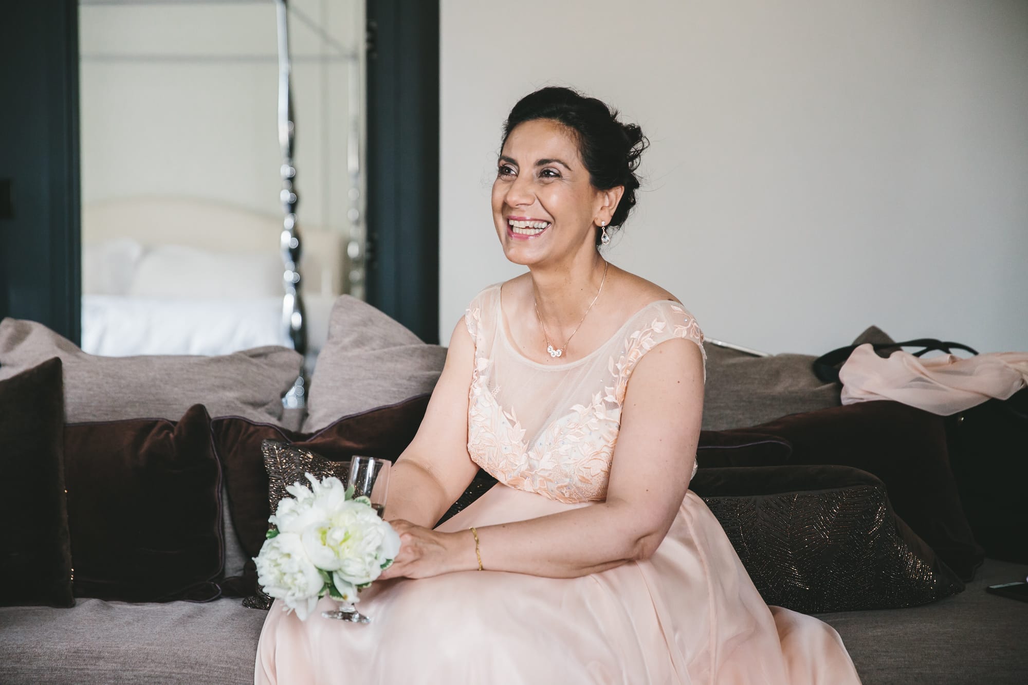 A documentary photograph of the mother of groom sitting on the couch before a State Room Wedding in Boston, Massachusetts