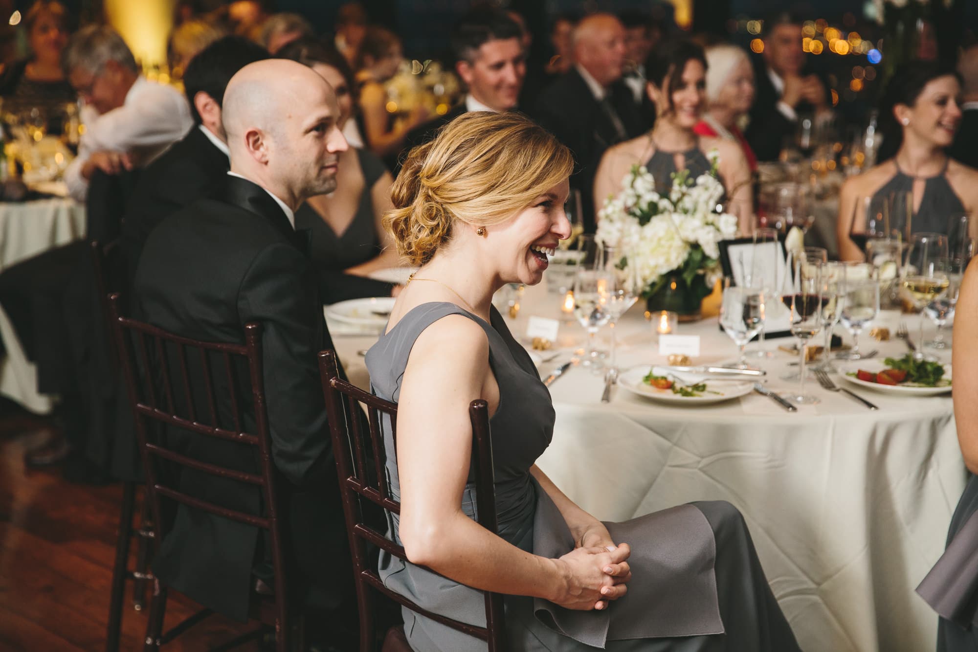 A documentary photograph of guests laughing during the speeches at a state room wedding reception