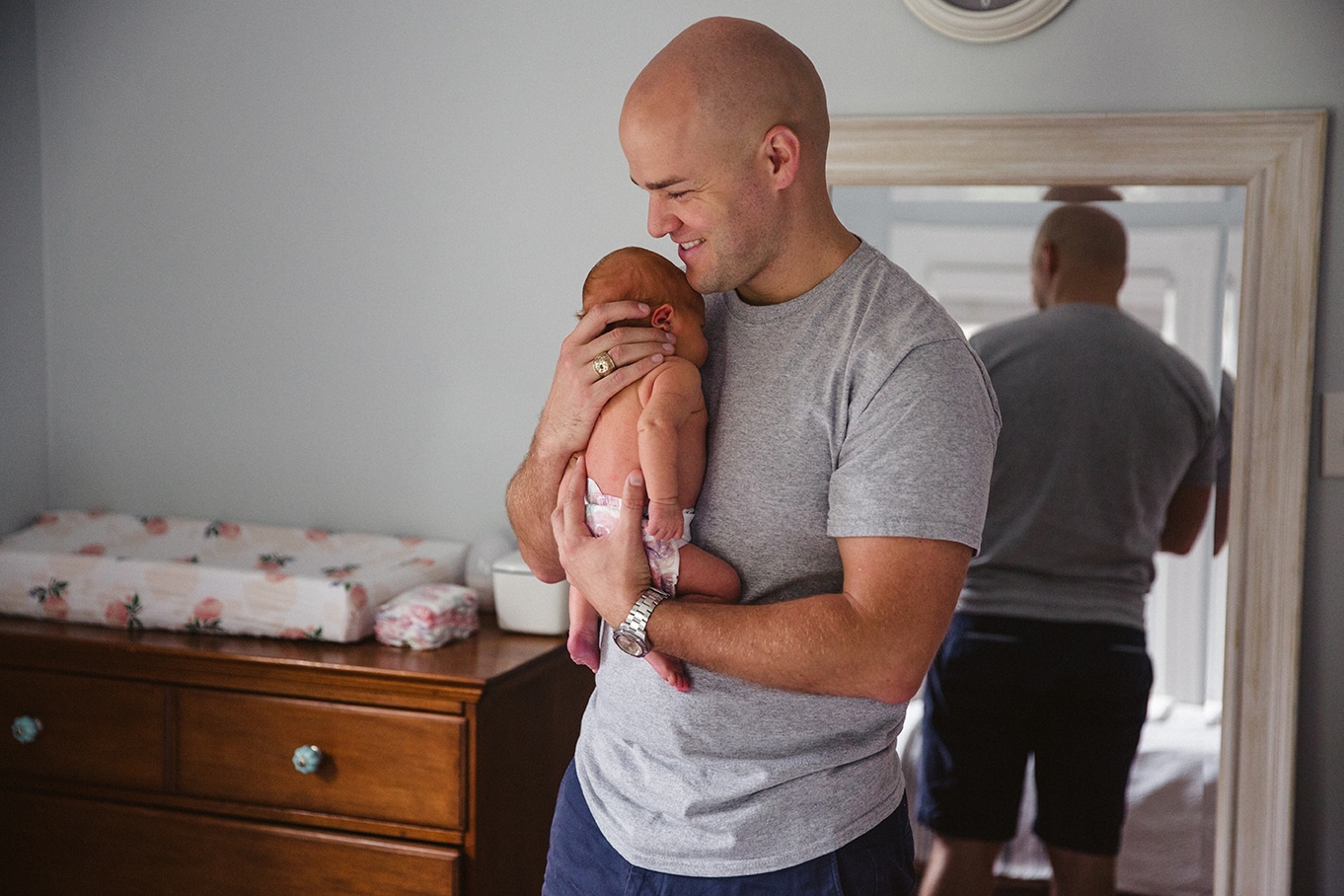 A documentary photograph of a father smiling as he holds his newborn daughter during their lifestyle newborn session in Boston, Massachusetts