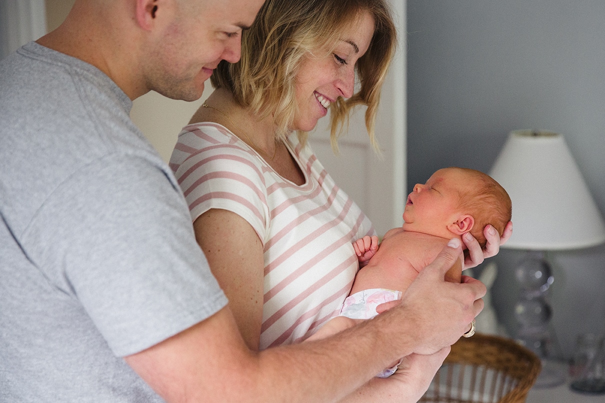 A documentary photograph of new parents smiling at their newborn daughter during their in home lifestyle newborn session in Boston, Massachusetts