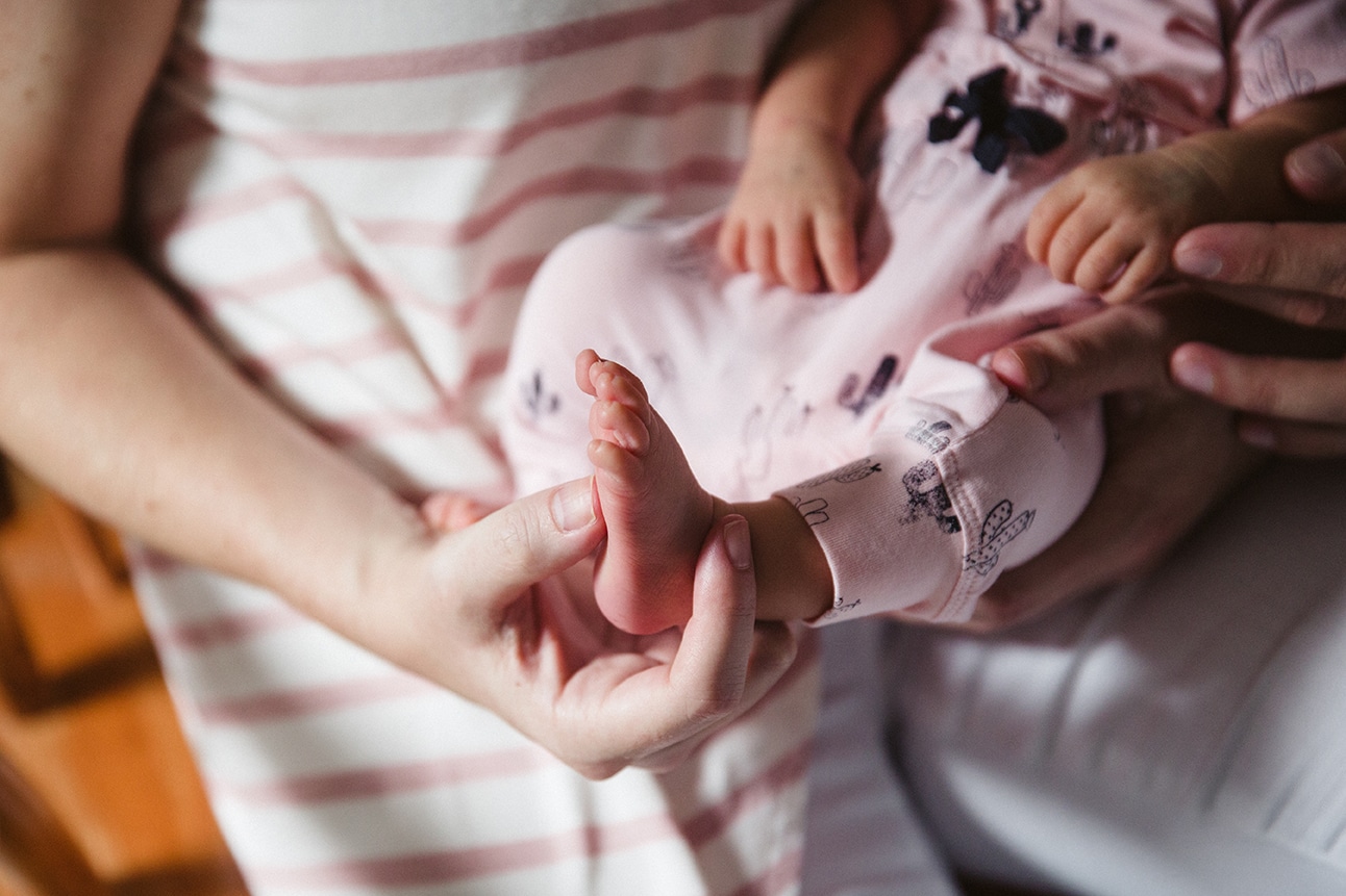 A documentary photograph of a new mom holding her newborn daughter's foot during their lifestyle session at home in Boston, Massachusetts