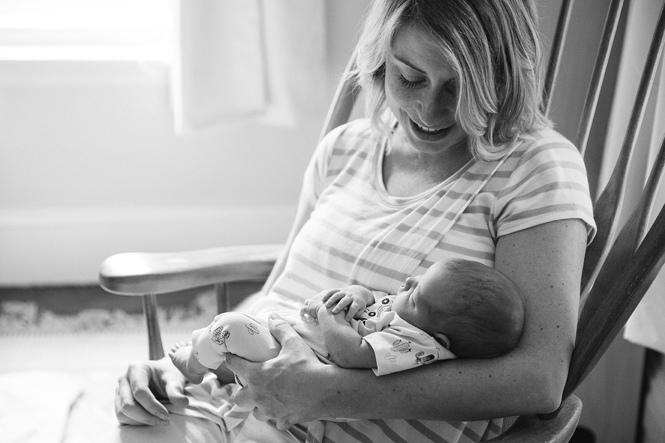 A documentary photograph of a new mom smiling at her newborn daughter as she rocks her to sleep during their in home lifestyle session in Boston, Massachusetts