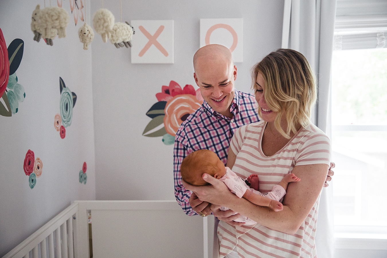 A documentary photograph of new parents smiling at their newborn daughter during their in home lifestyle session in Boston, Massachusetts