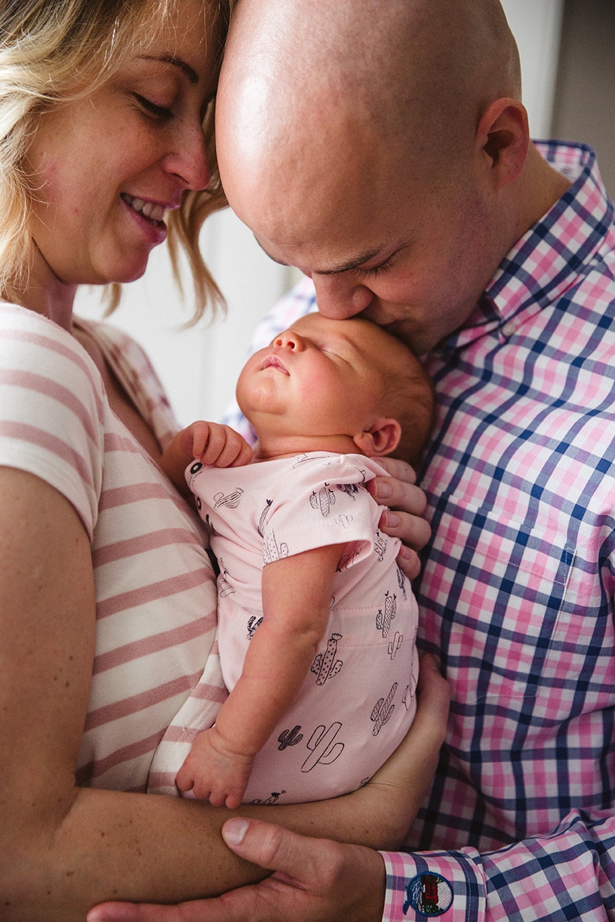 A documentary portrait of new parents holding and kissing their newborn daughter during an in home lifestyle session in Boston, Massachusetts