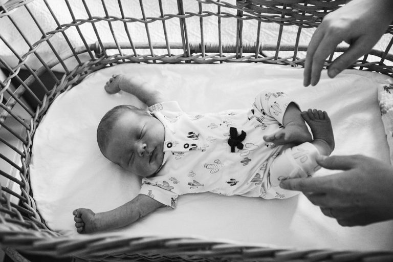 newborn stretches as her mother places her in to her bassinet during their lifestyle newborn session in Boston, Massachusetts
